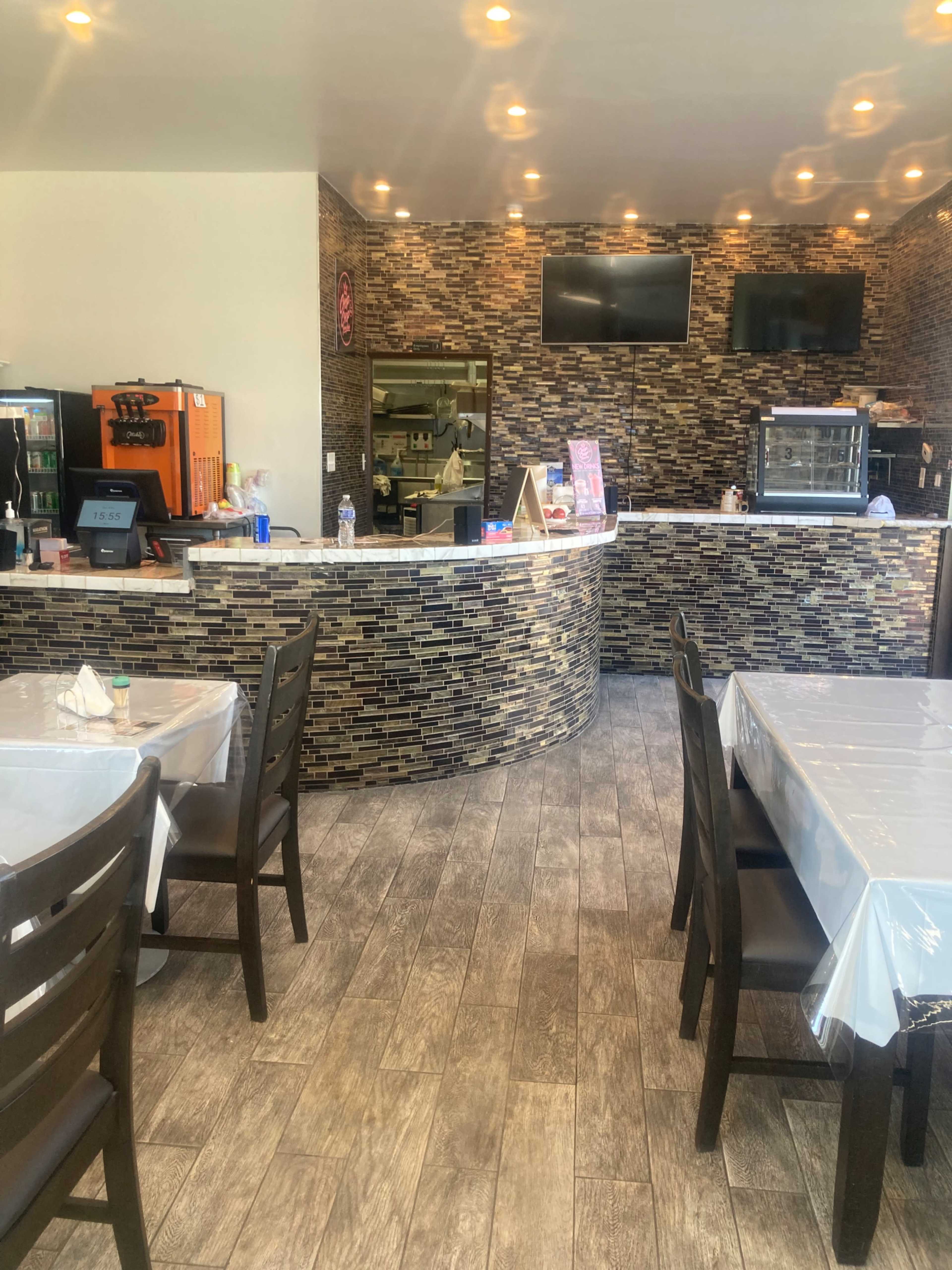 The image shows a modern restaurant interior with a curved service counter, several tables covered with white tablecloths, and stone-patterned walls.