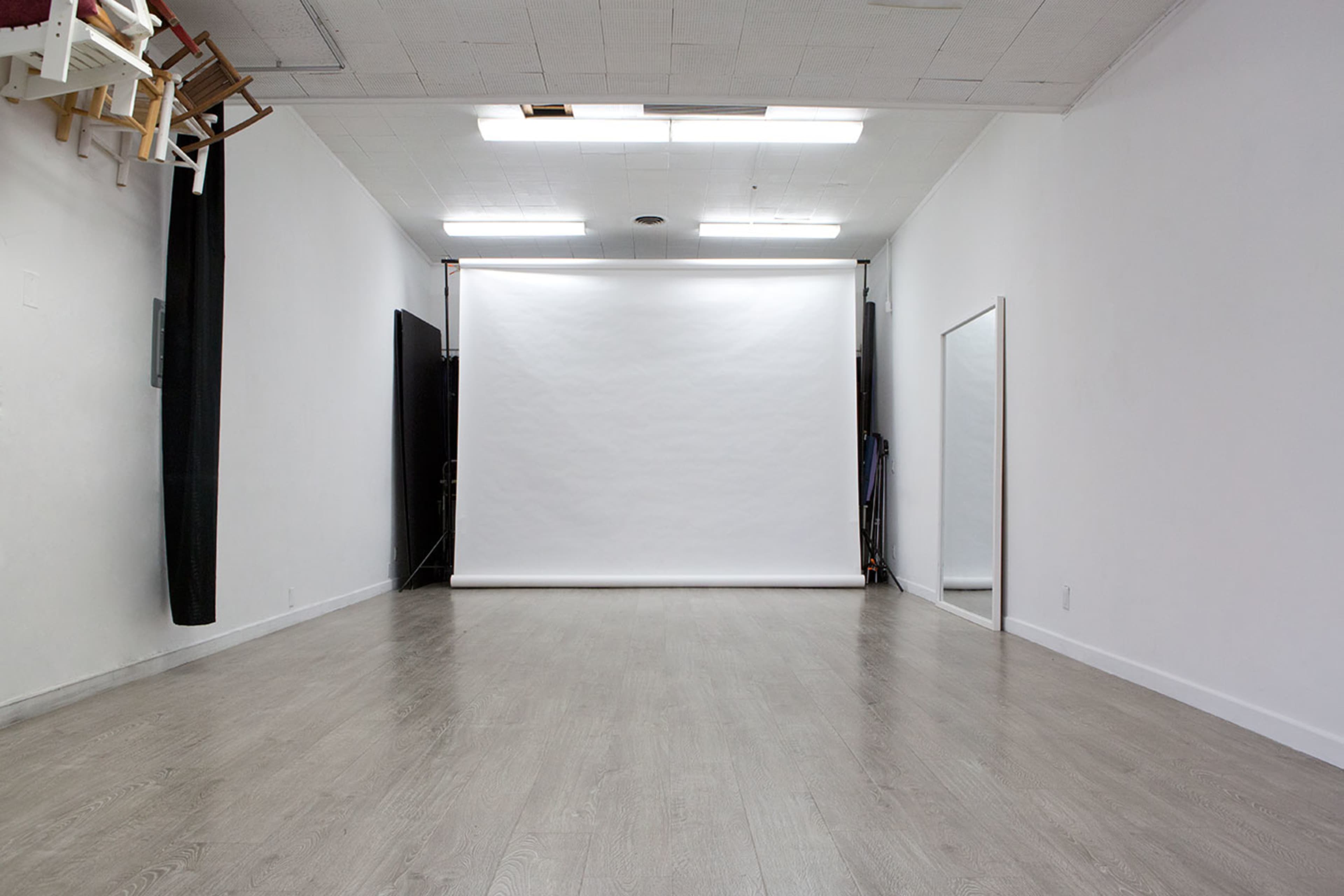 A spacious, empty room with white walls, a large white backdrop, and a mirror on one side.