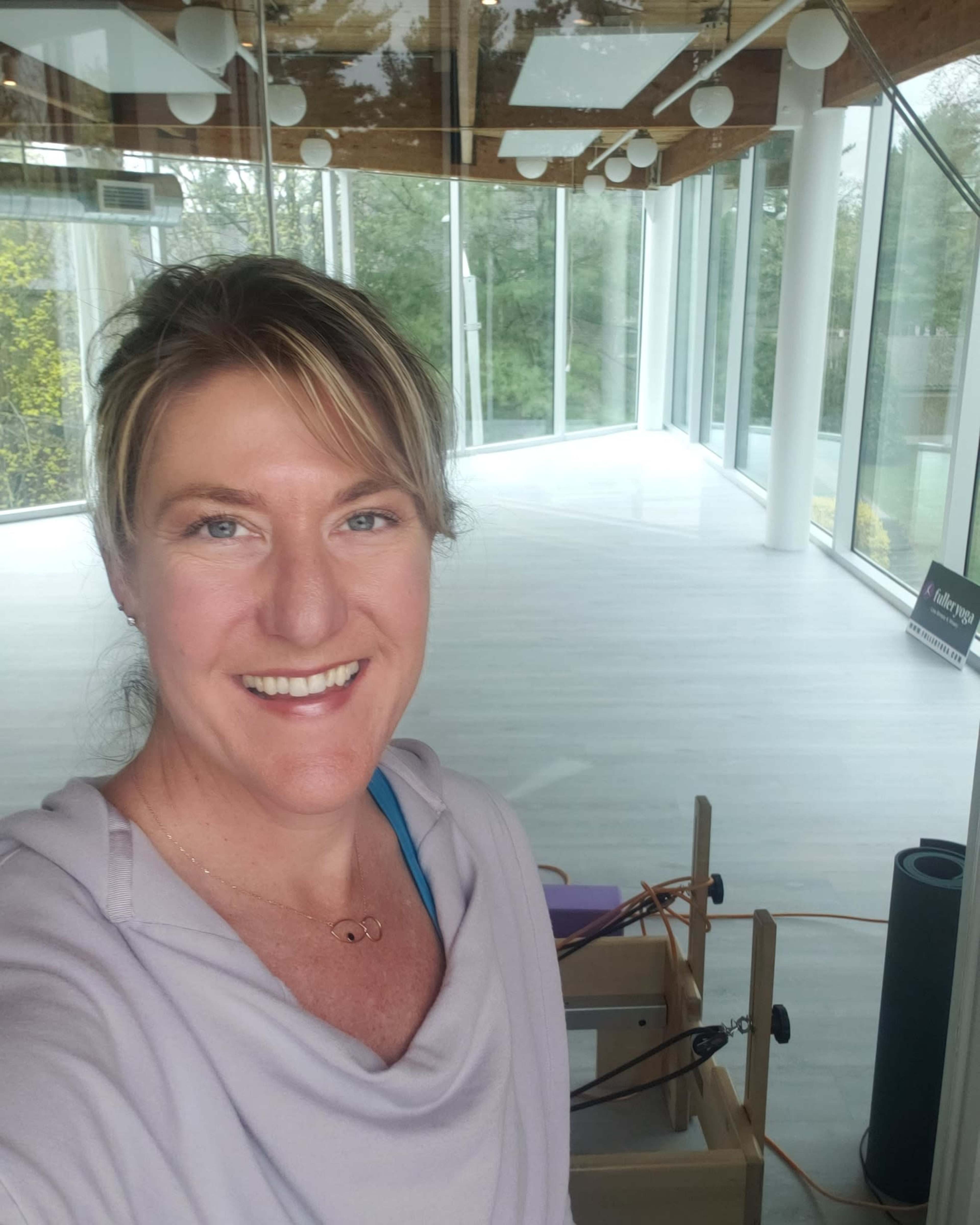 A woman smiles in a bright, modern studio with large windows and minimalistic decor.