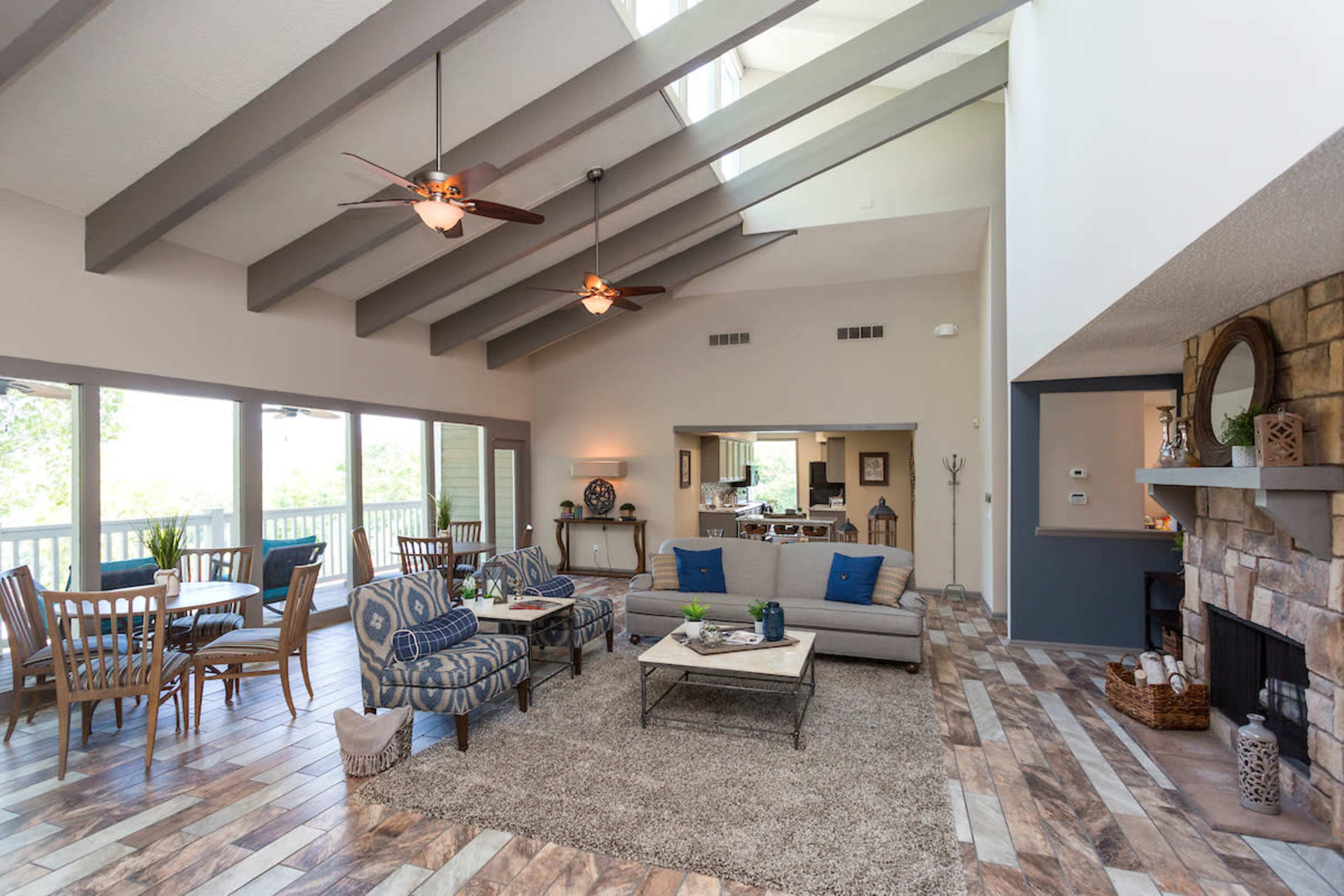 A spacious living room with high ceilings, large windows, and a cozy seating area furnished with a gray sofa and patterned chairs.