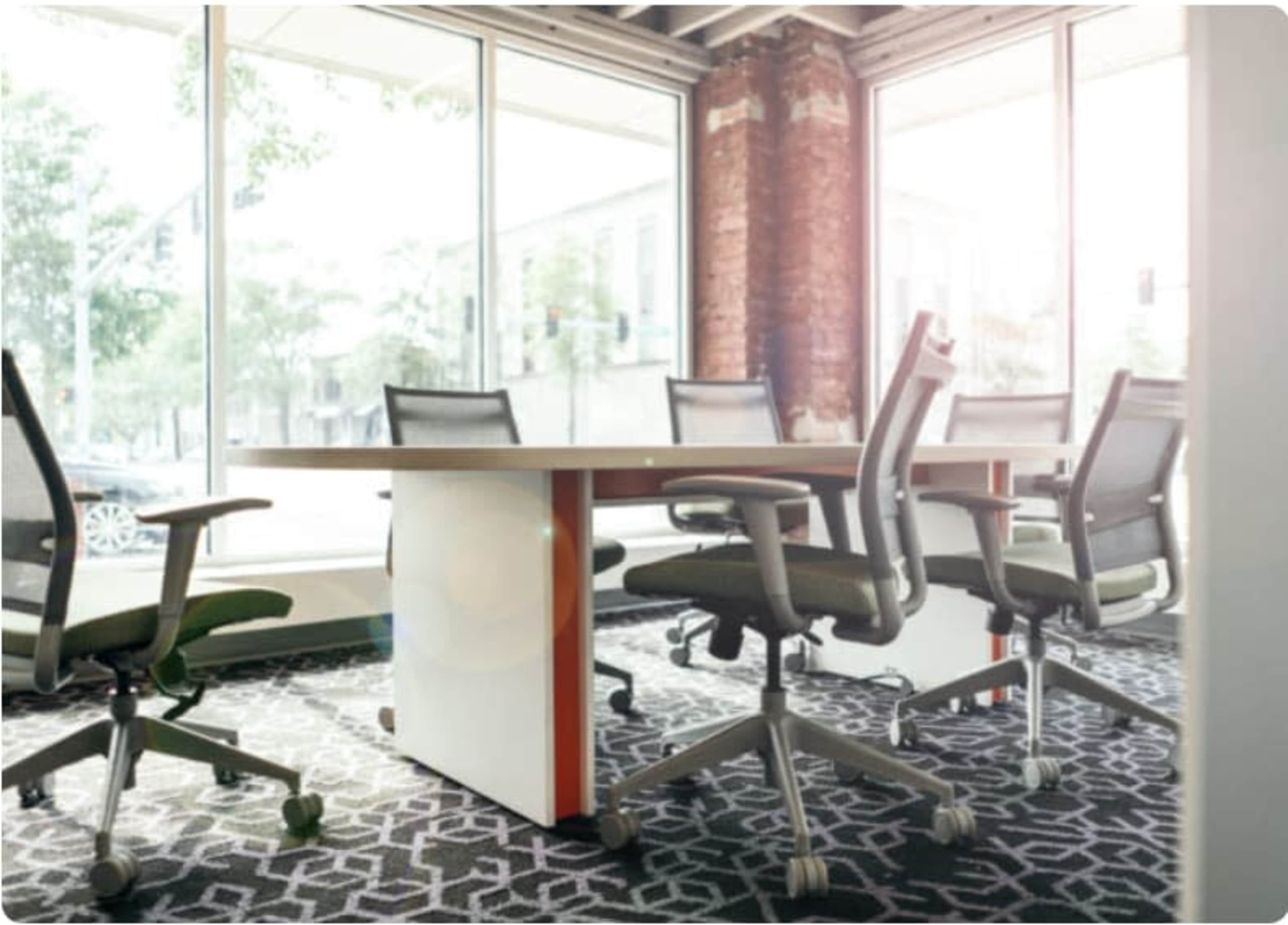 A spacious conference room features a large table surrounded by several ergonomic chairs, with large windows allowing natural light to illuminate the space.