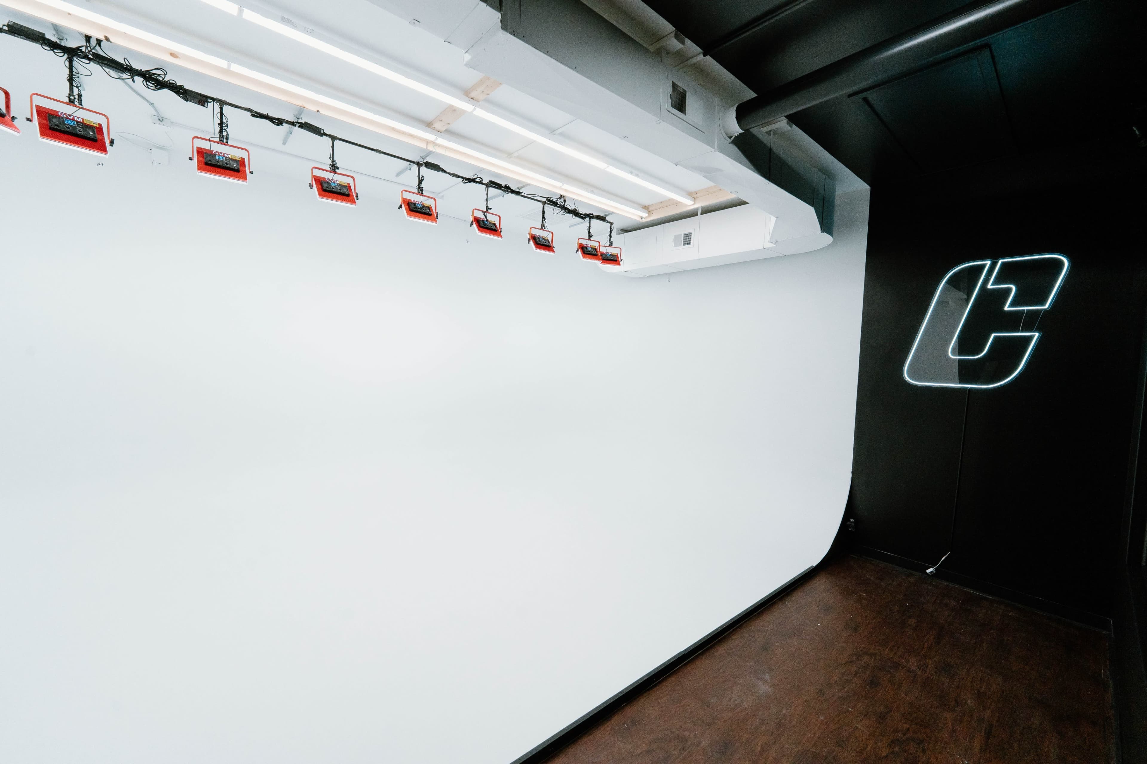 The image shows a minimalist studio space with a white backdrop and multiple red lights suspended from the ceiling.