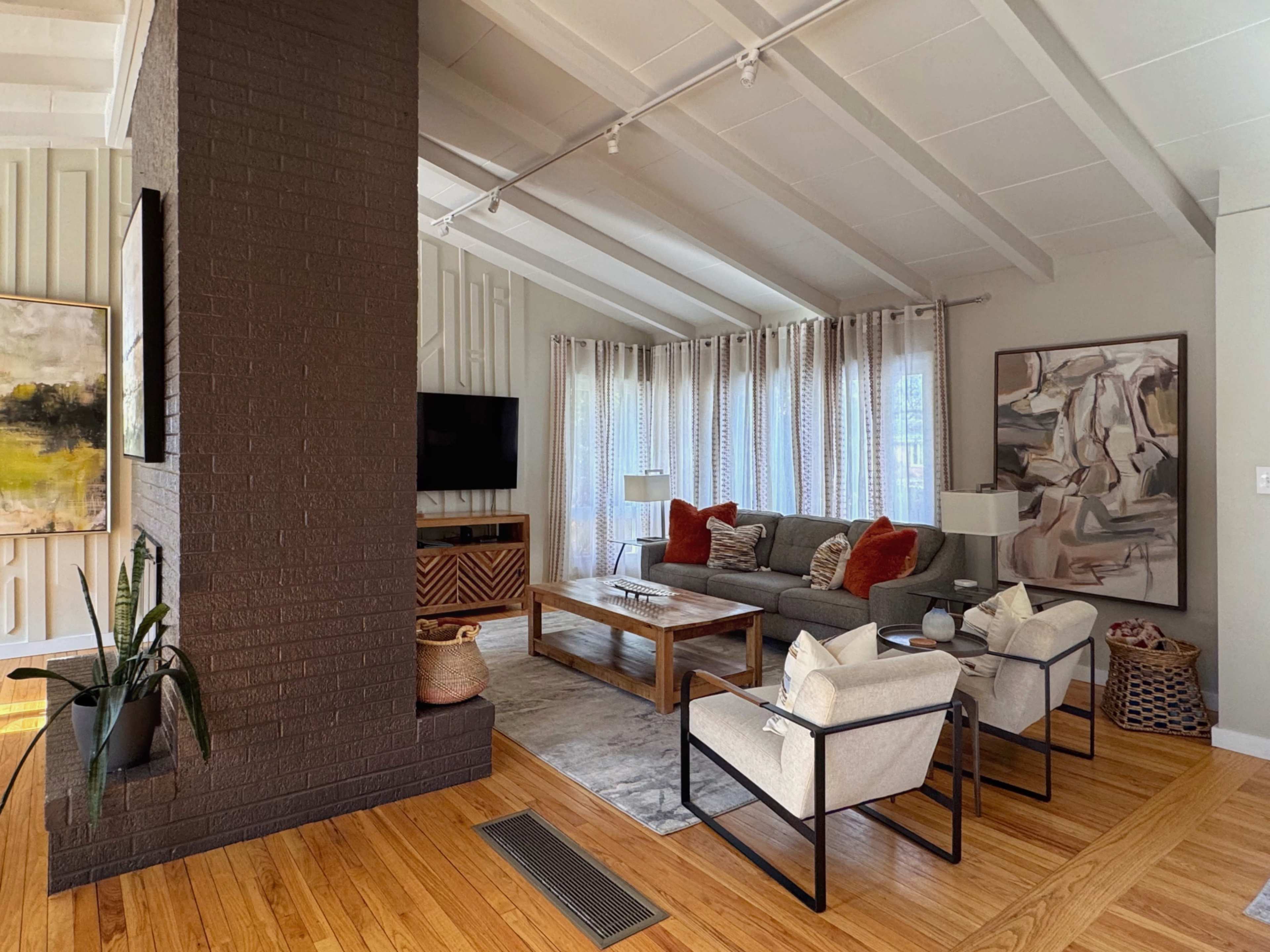 The image shows a modern living room featuring a large sofa with decorative pillows, two armchairs, a coffee table, and a textured accent wall, all enhanced by natural light coming through large windows.