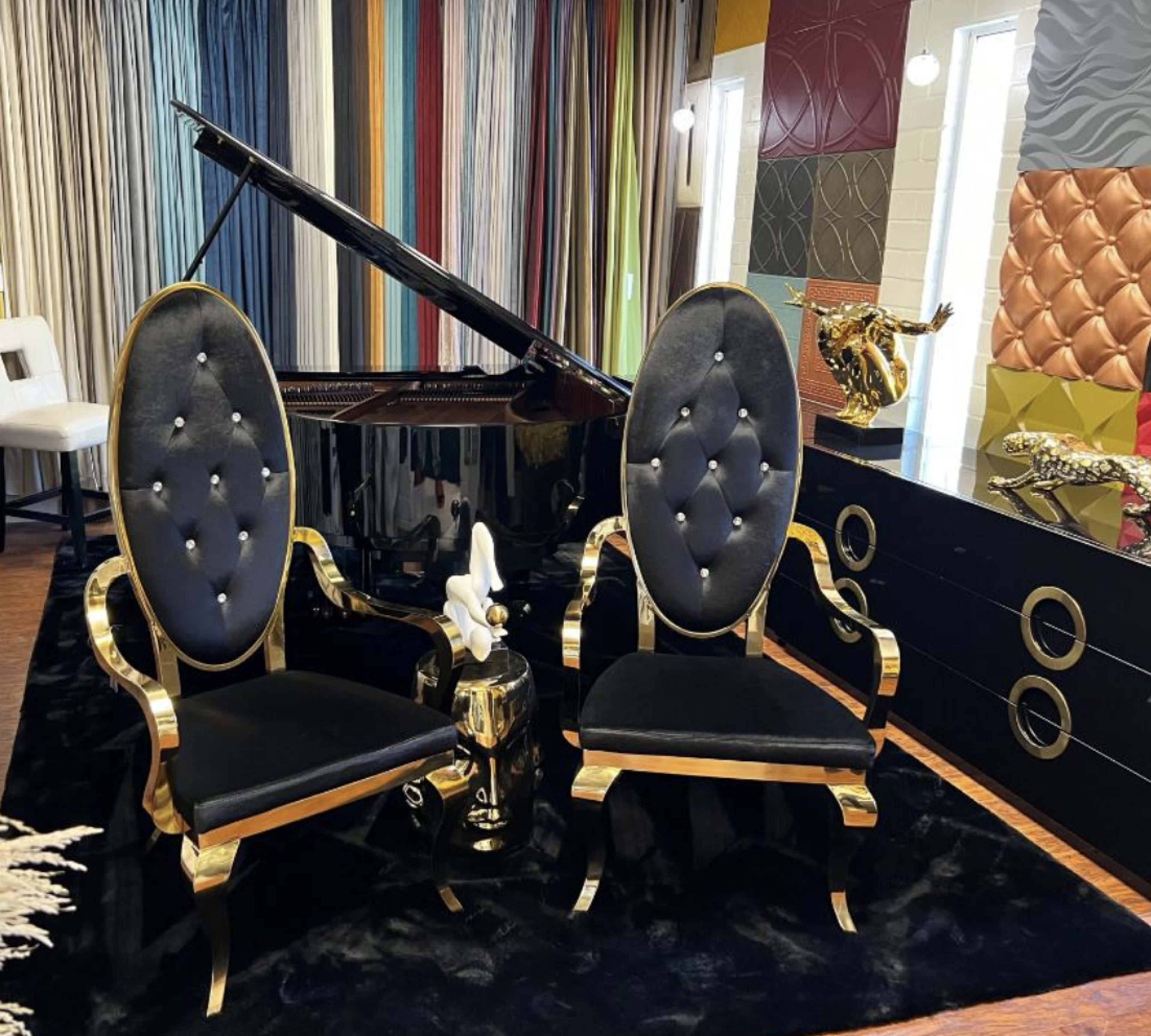 Two ornate black and gold chairs are positioned in front of a grand piano, accompanied by a decorative sculpture and a colorful wall display.