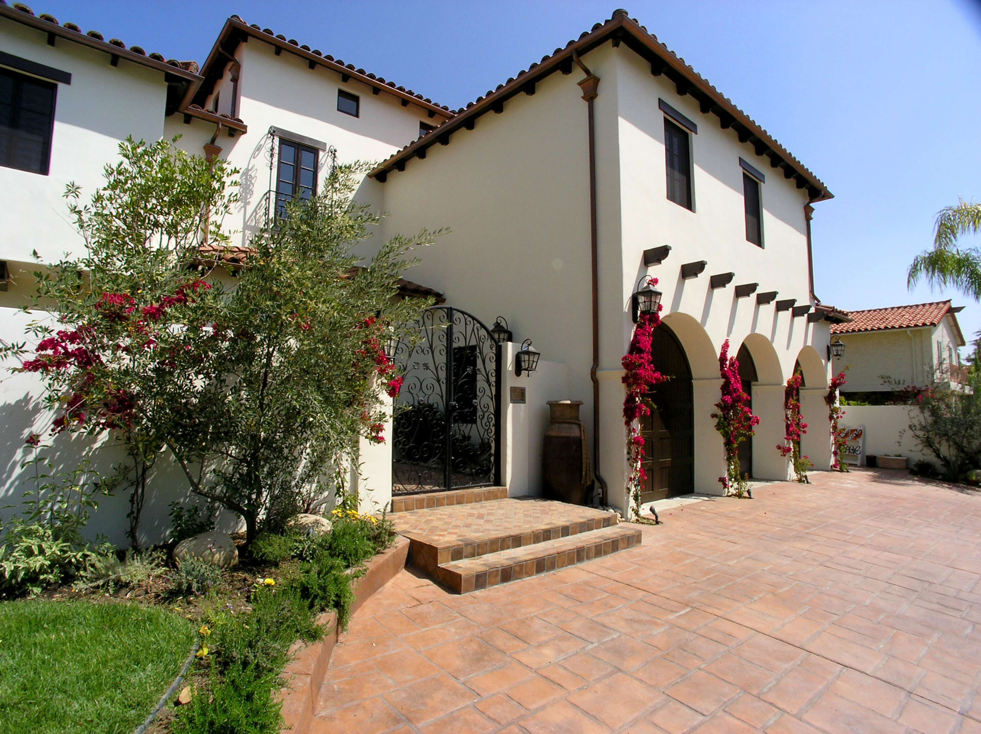 A two-story house with a stucco facade, wrought iron gate, and flowering vines along the entrance.