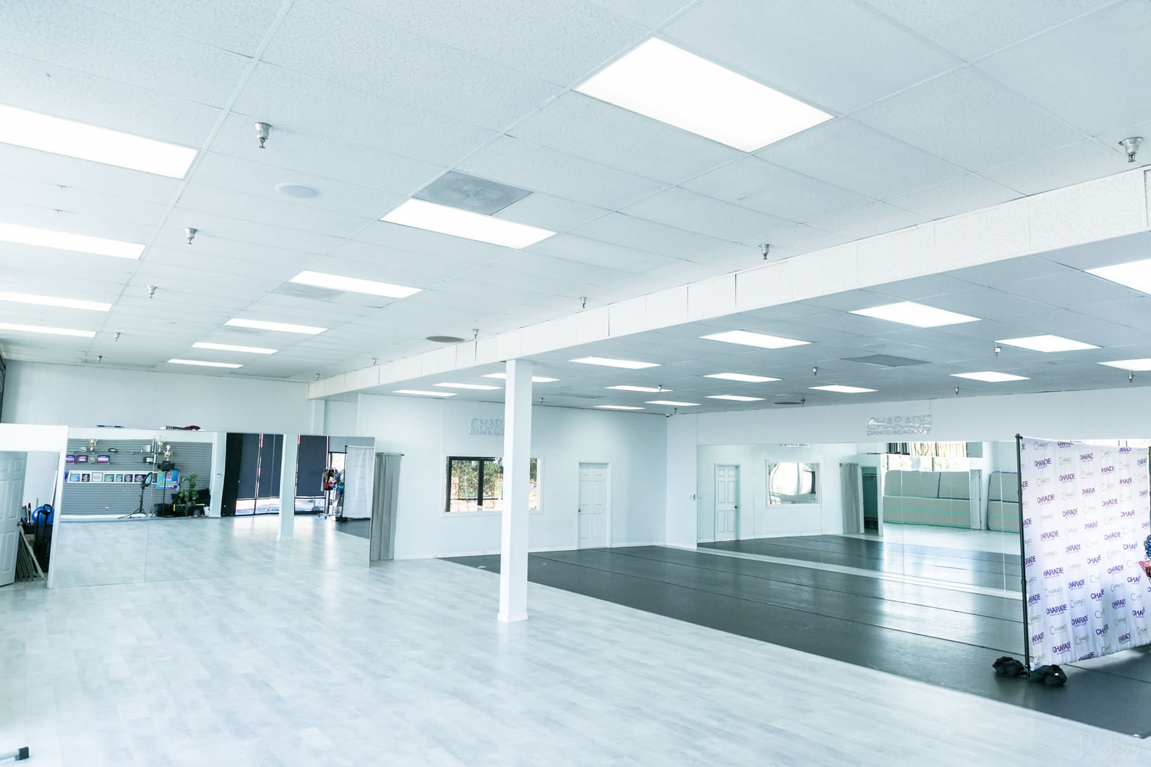 The image shows a spacious dance studio with mirrored walls, wooden flooring, and bright overhead lighting.
