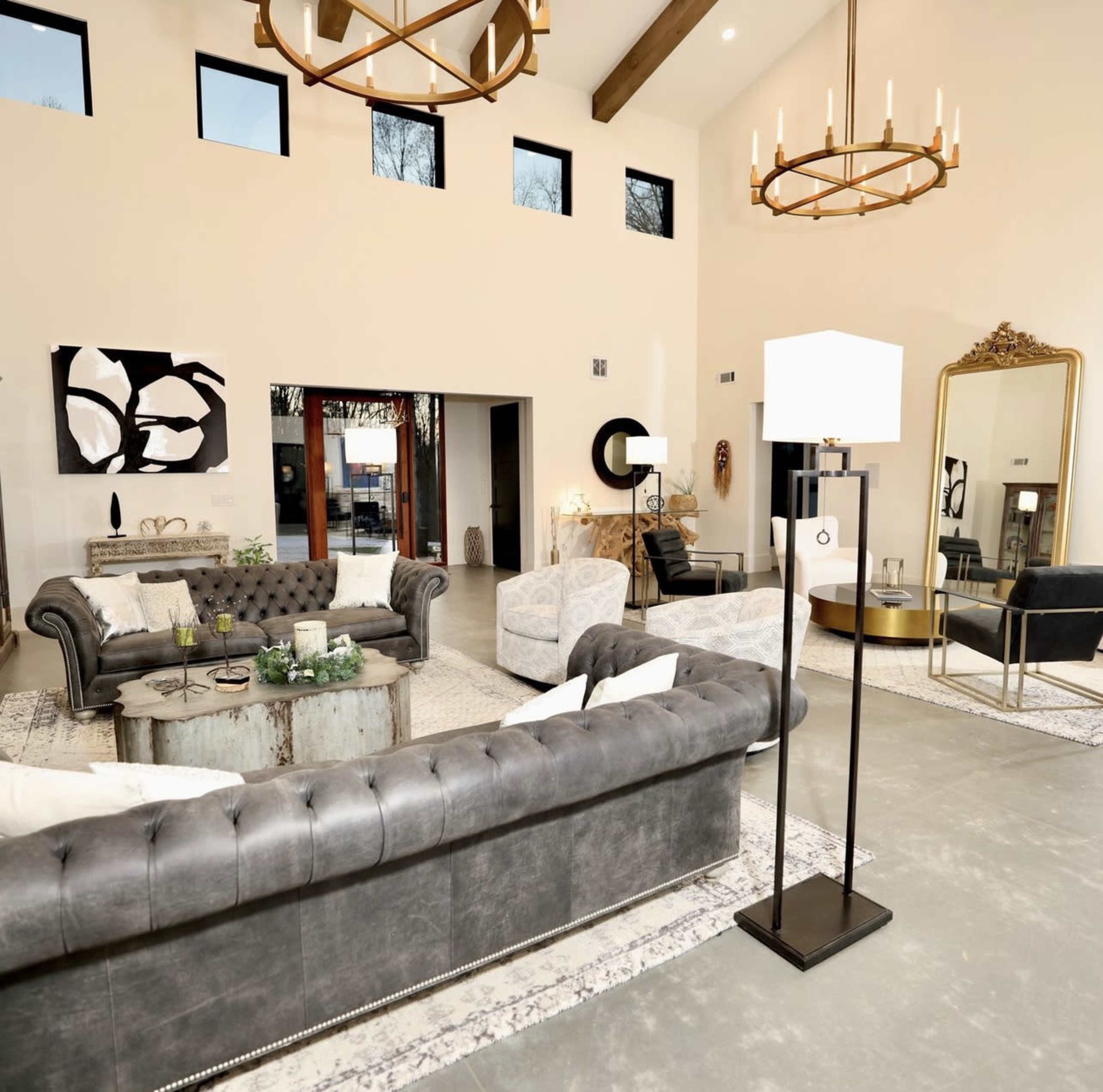 A modern living room with gray leather sofas, a coffee table, a standing lamp, and large windows illuminating the space.