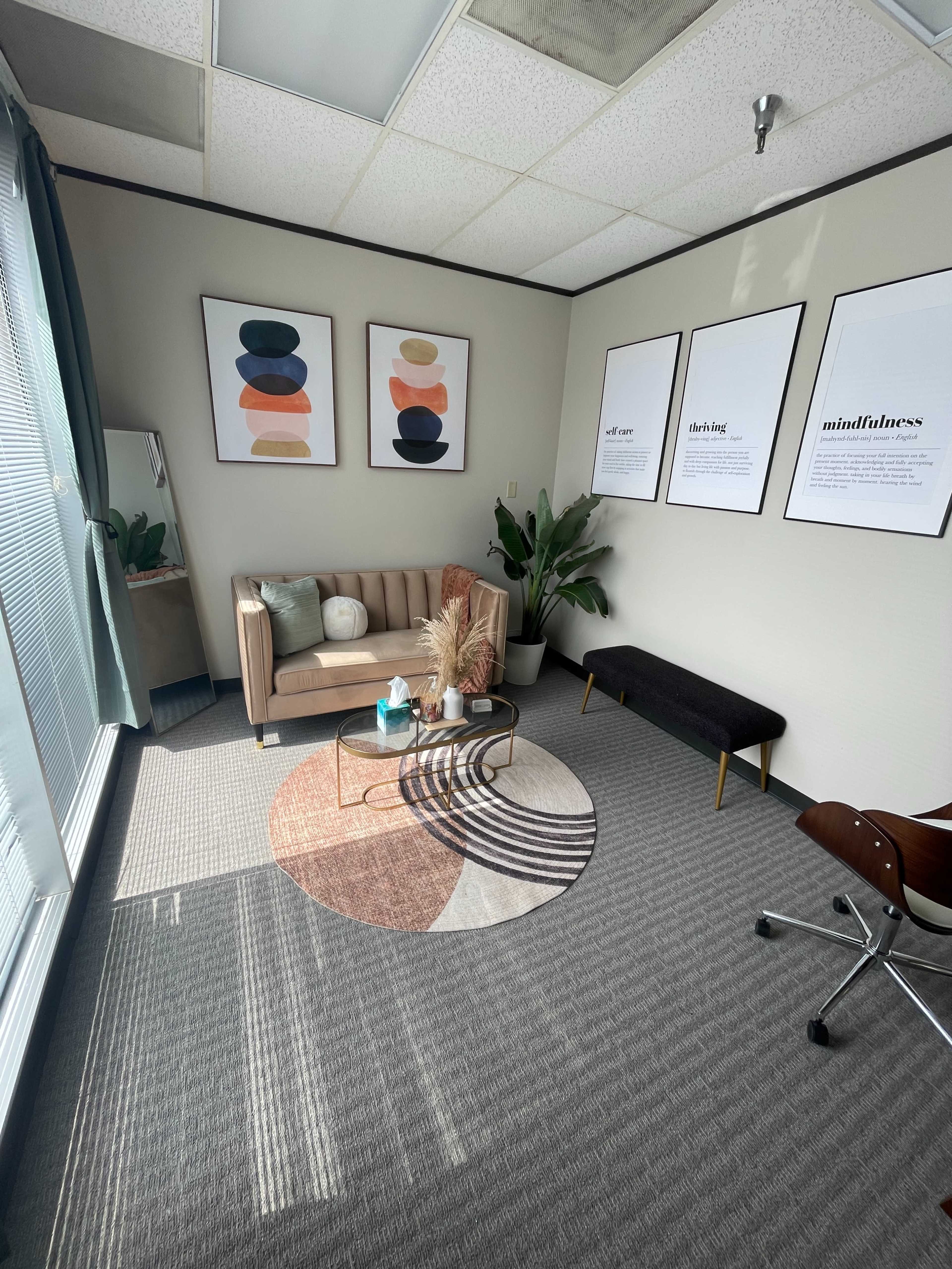A well-furnished office space featuring a beige couch, a round area rug, wall art, and indoor plants.