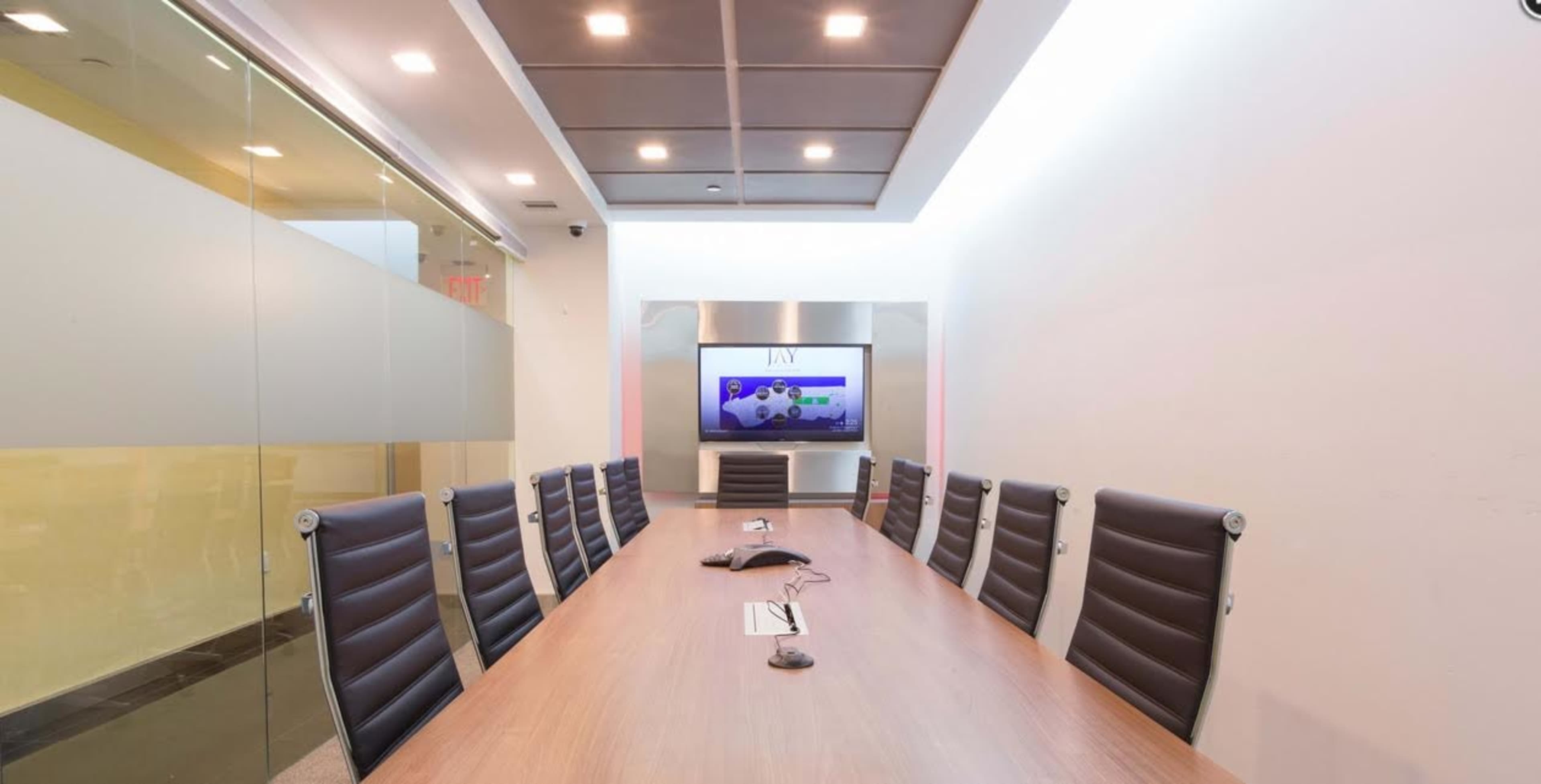 A modern conference room features a long wooden table, leather chairs, and a large screen at one end.