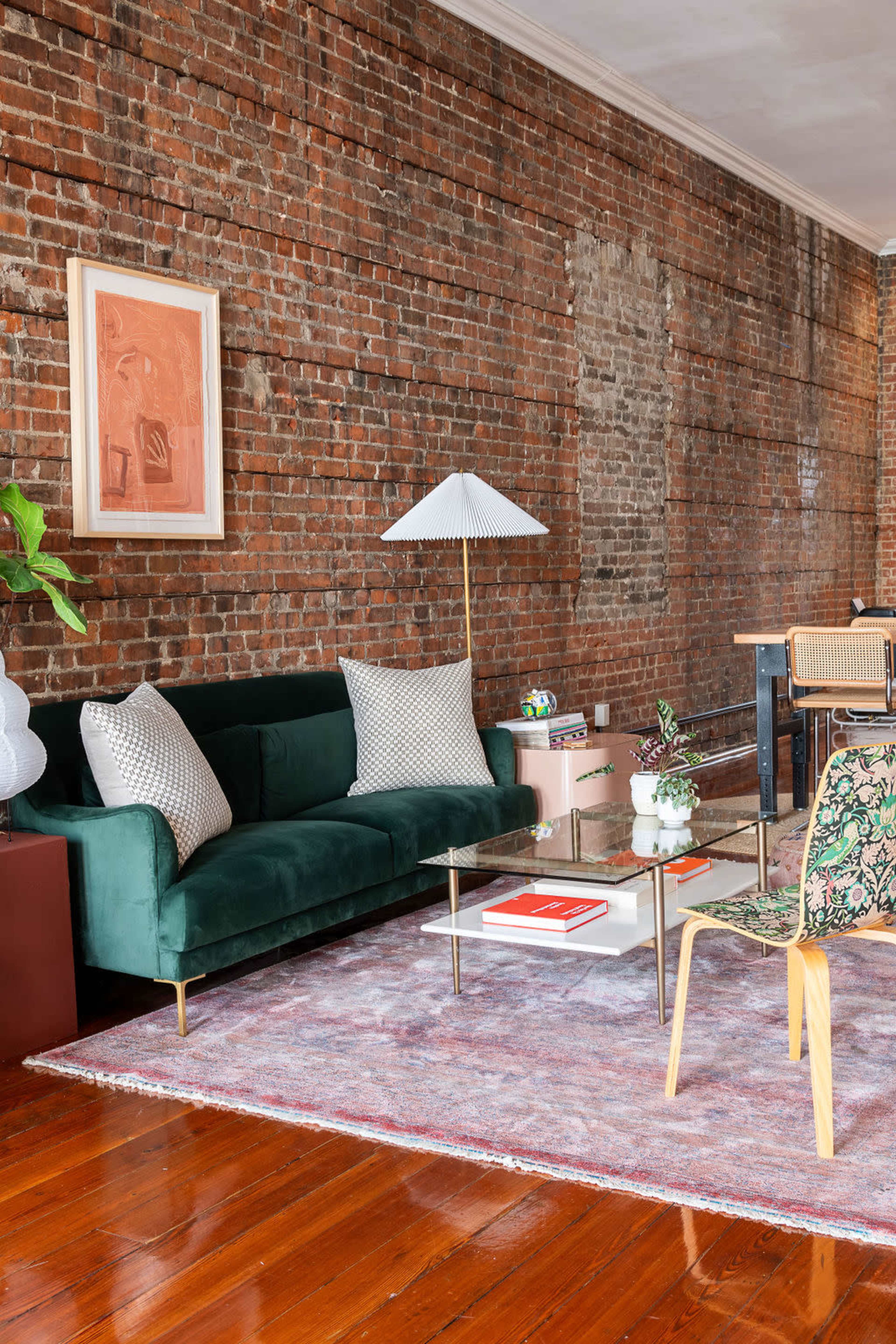 A modern living room with a green sofa, a glass coffee table, a decorative lamp, and a brick wall backdrop.