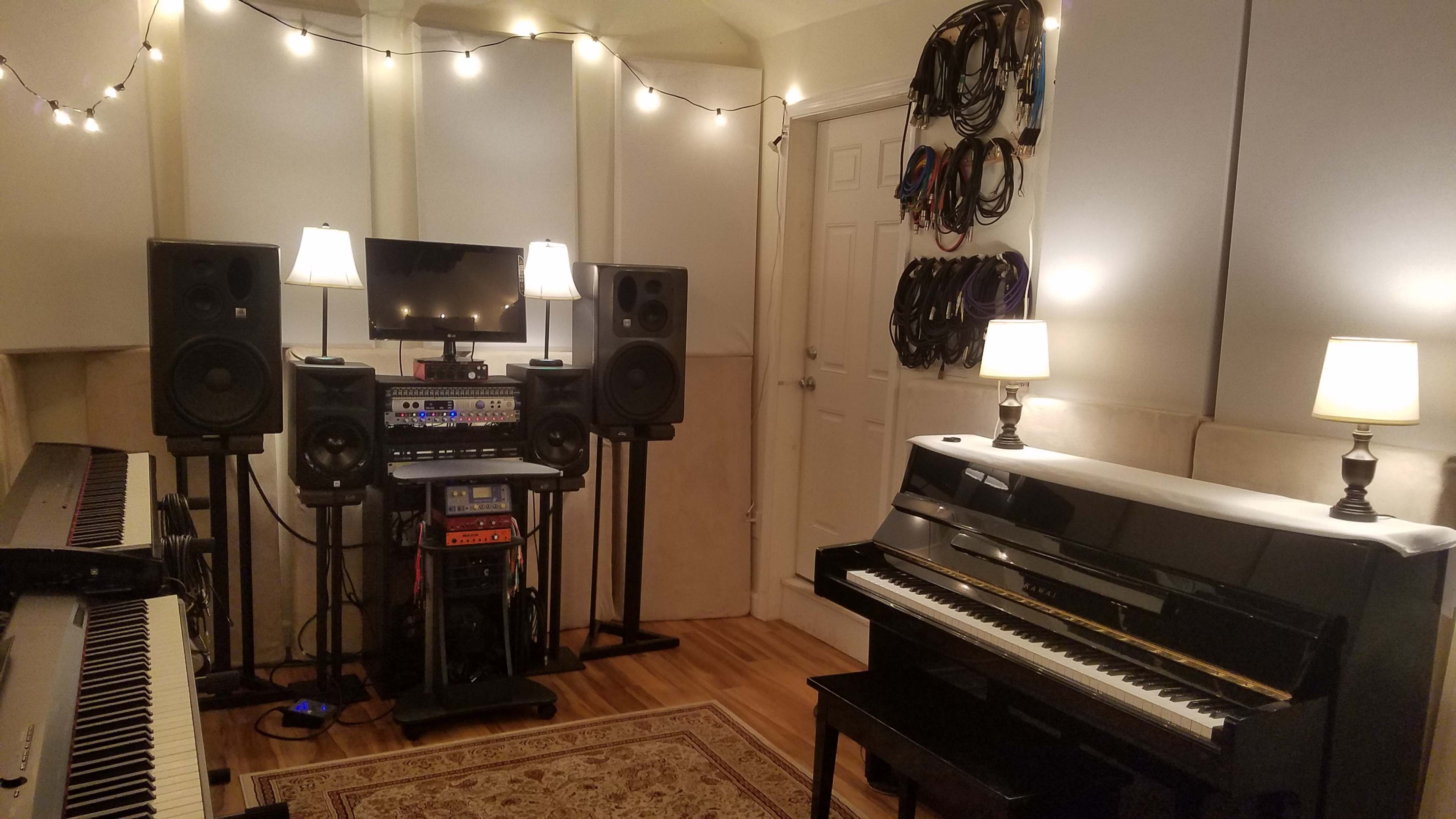 A music studio with a digital piano, an acoustic piano, audio speakers, a mixing console, and ambient lighting.