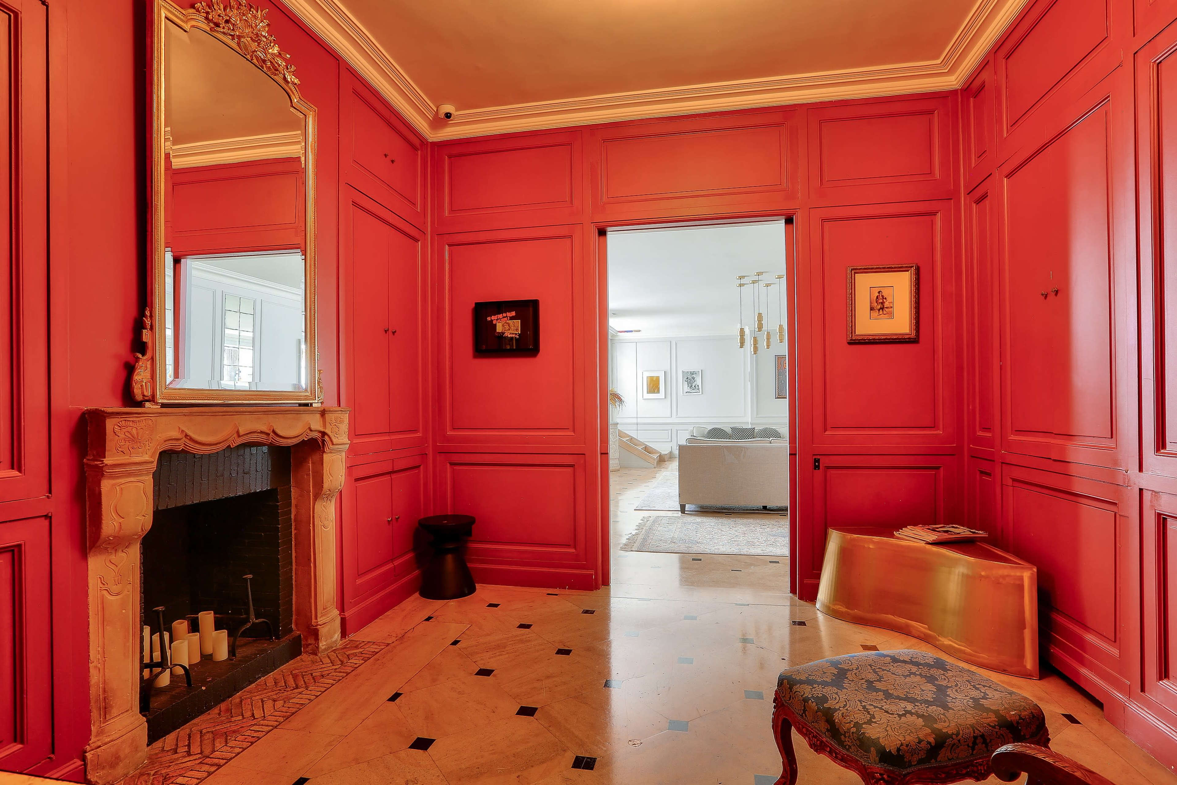 The image shows a hallway with red paneled walls, a decorative mirror, a fireplace, and a doorway leading to a bright living area.