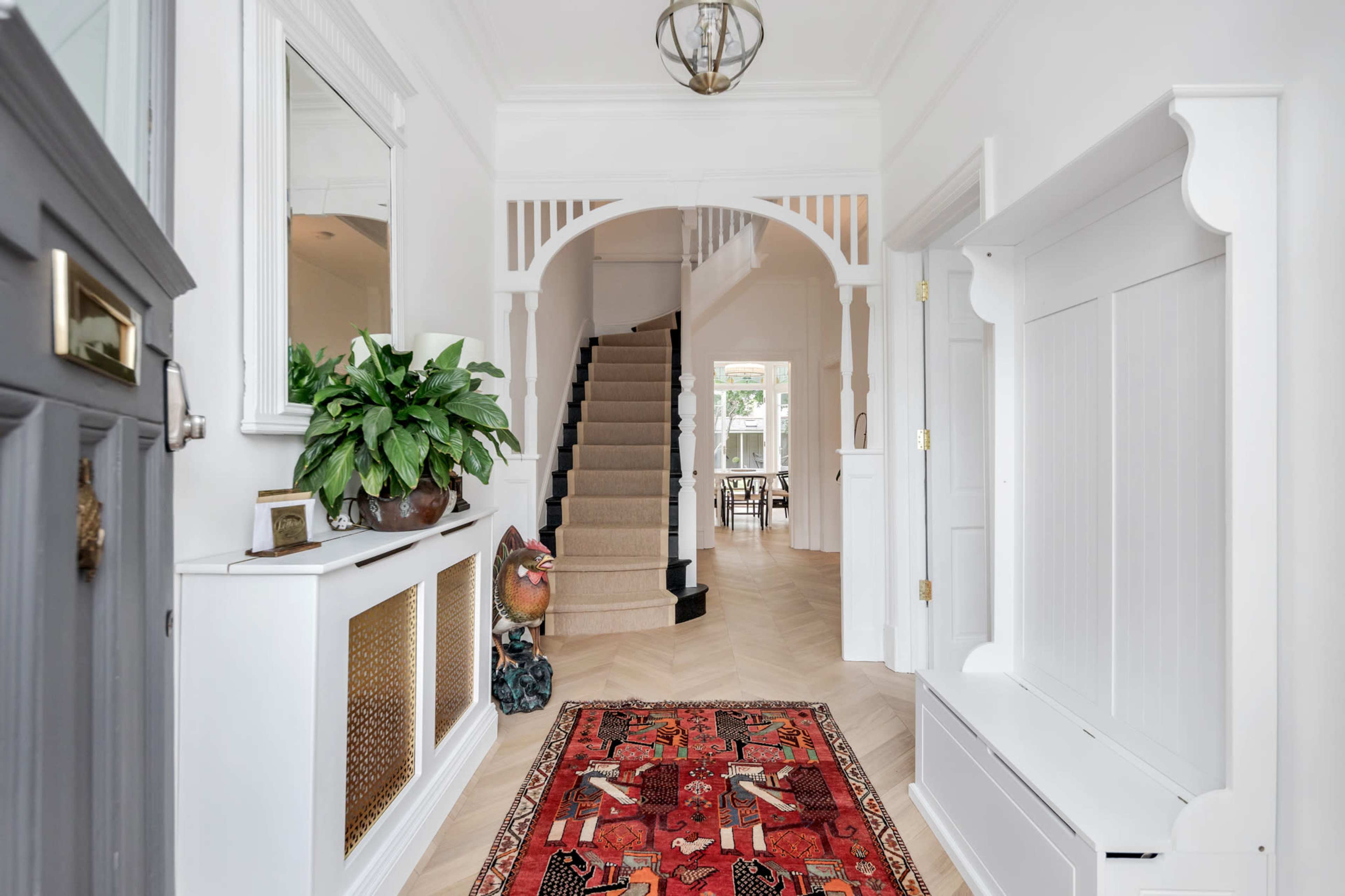 A bright entryway featuring a staircase, a decorative rug, a potted plant, and a wall mirror.