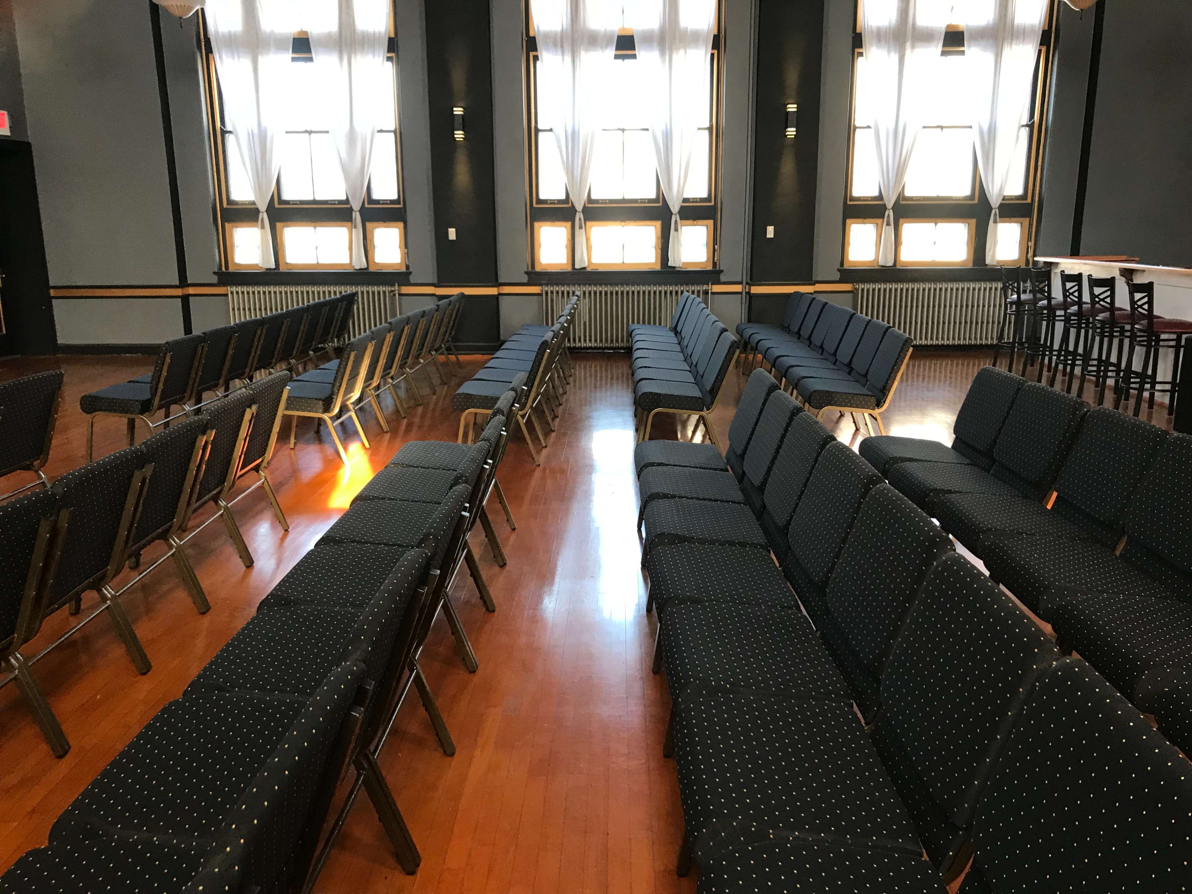 A row of dark blue chairs with polka dot fabric is arranged parallel to one another in a well-lit, spacious room with tall windows.