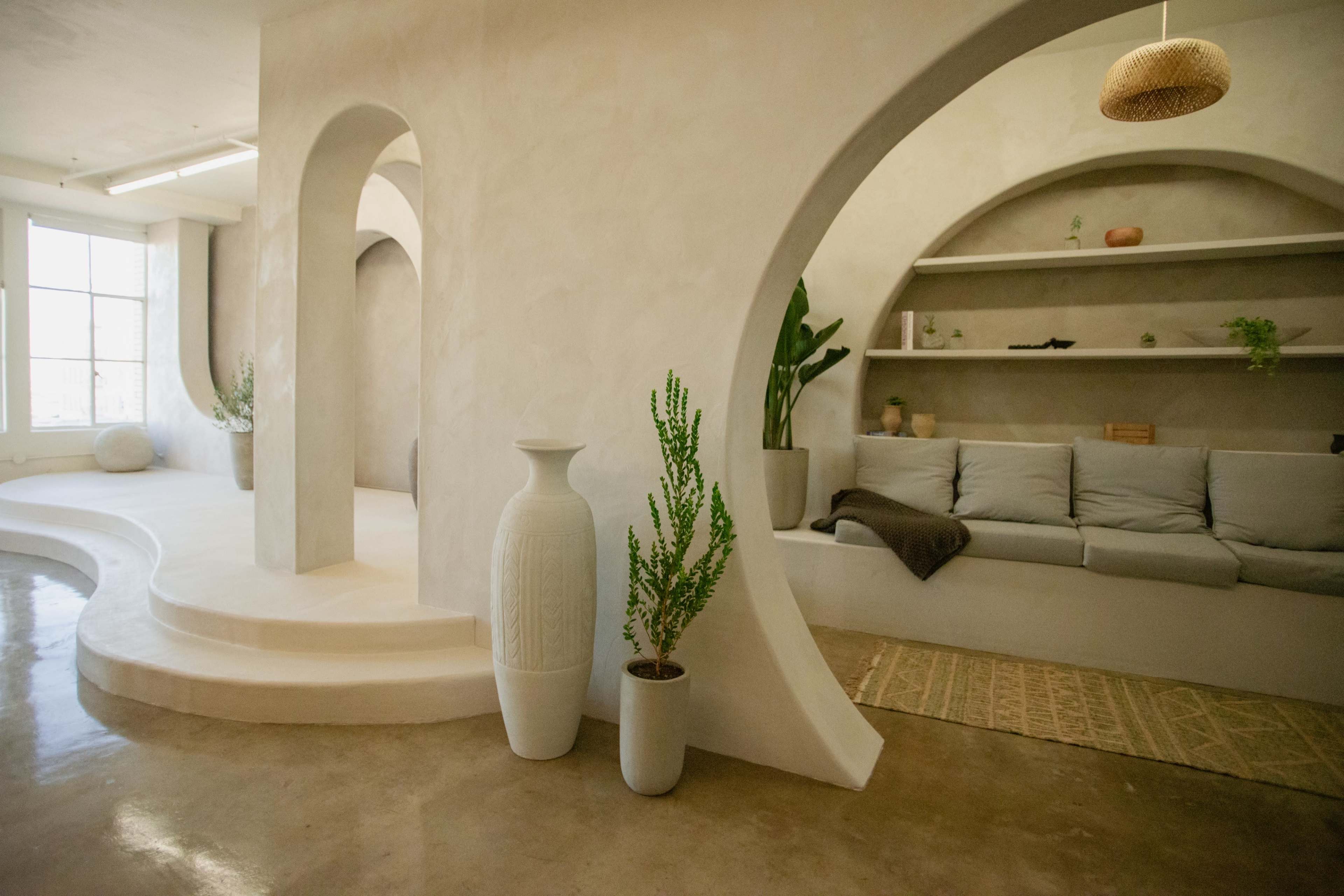 A minimalist interior space featuring curved architectural elements, a light-colored palette, and a seating area with plants and decorative items.