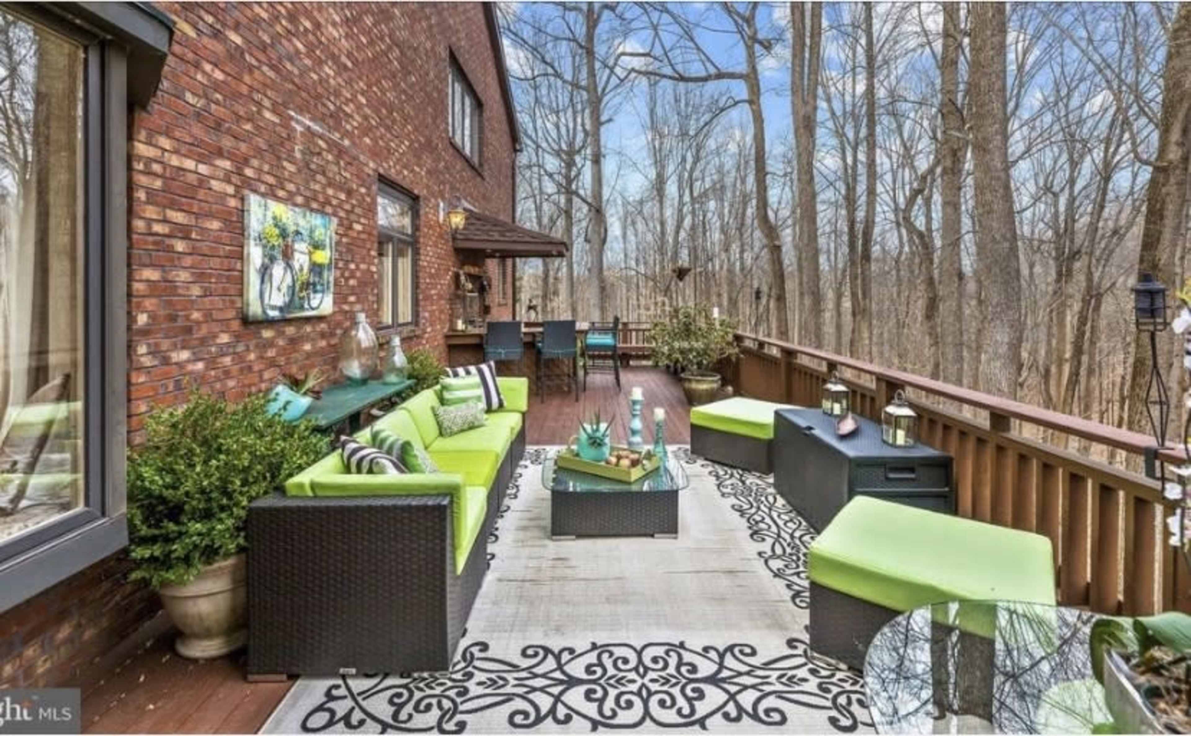 A deck featuring green outdoor furniture, a patterned rug, and a wooded area in the background.