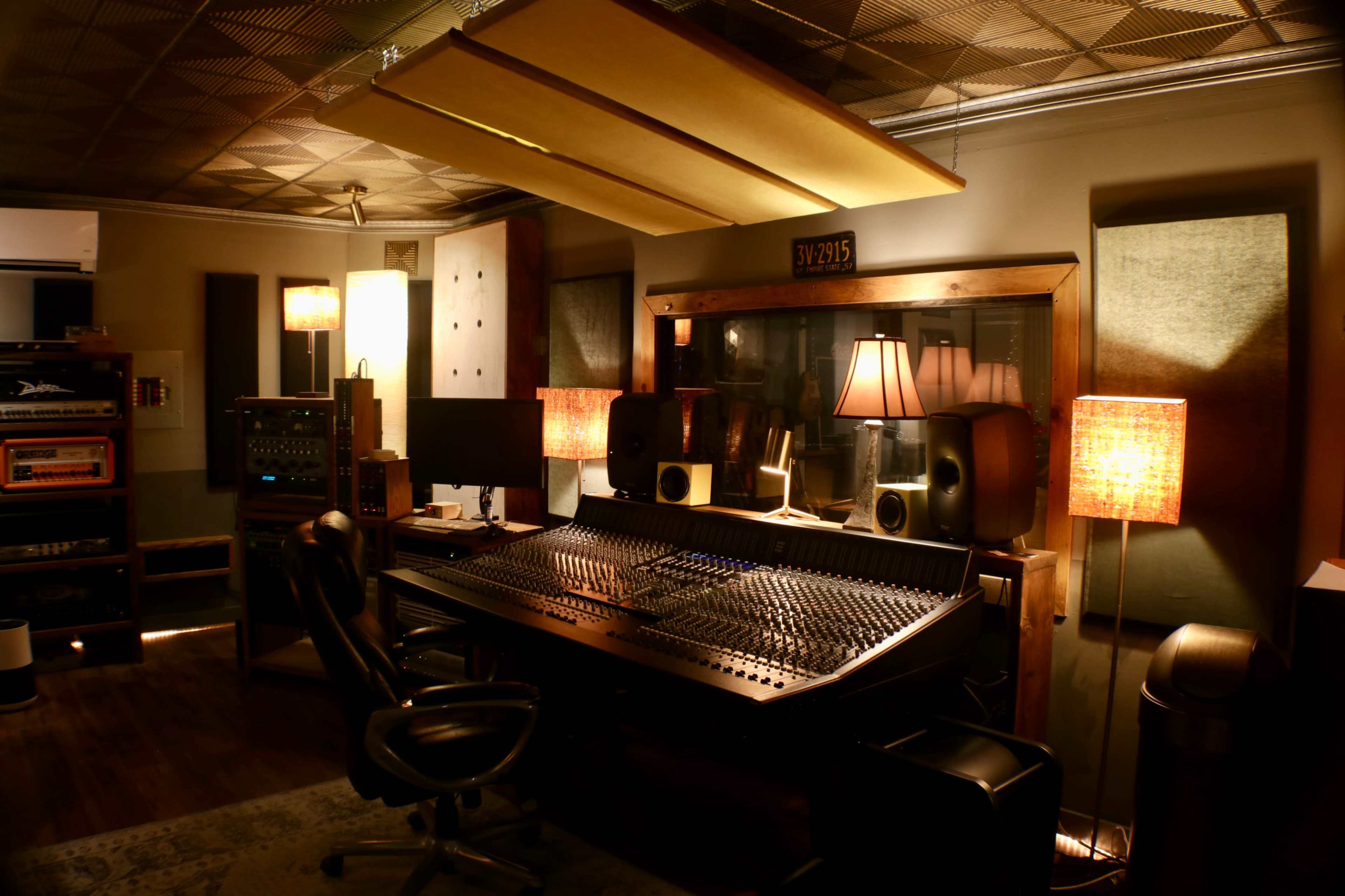 A dimly lit recording studio featuring a large mixing console, speakers, and ambient lamps.