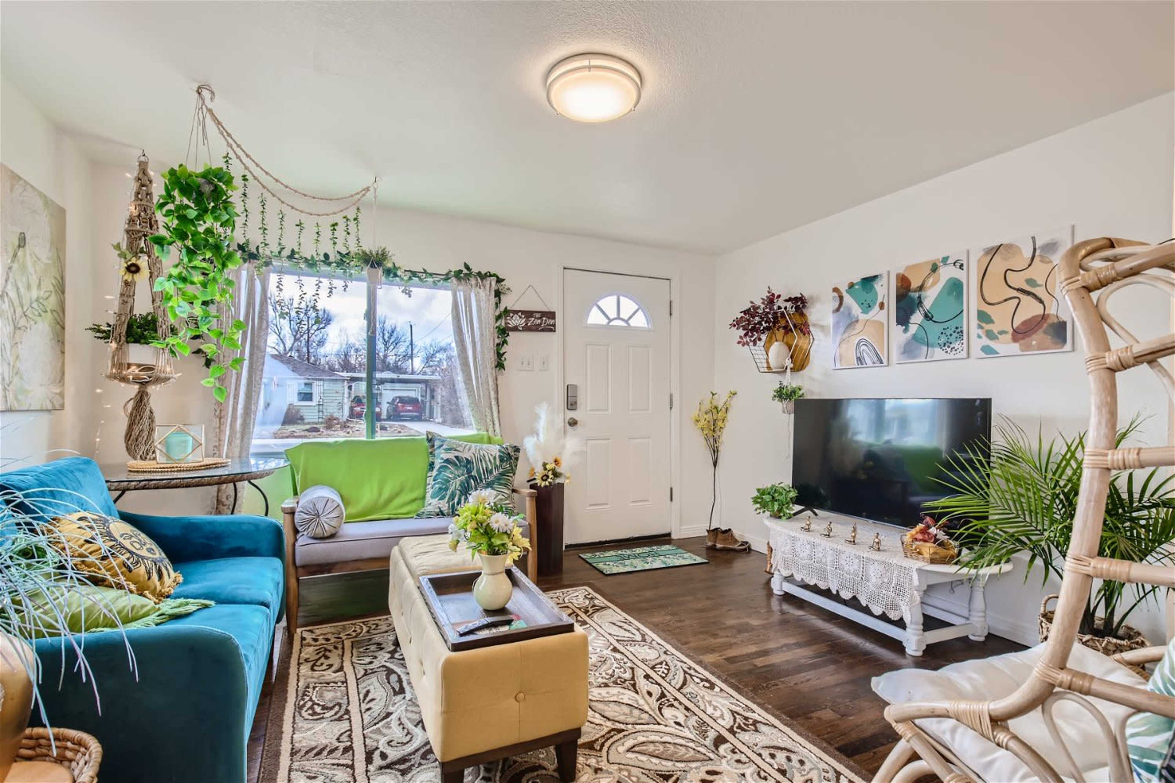 The living room features a mix of colorful furniture, plants, and wall art, with a television placed on a decorative console.