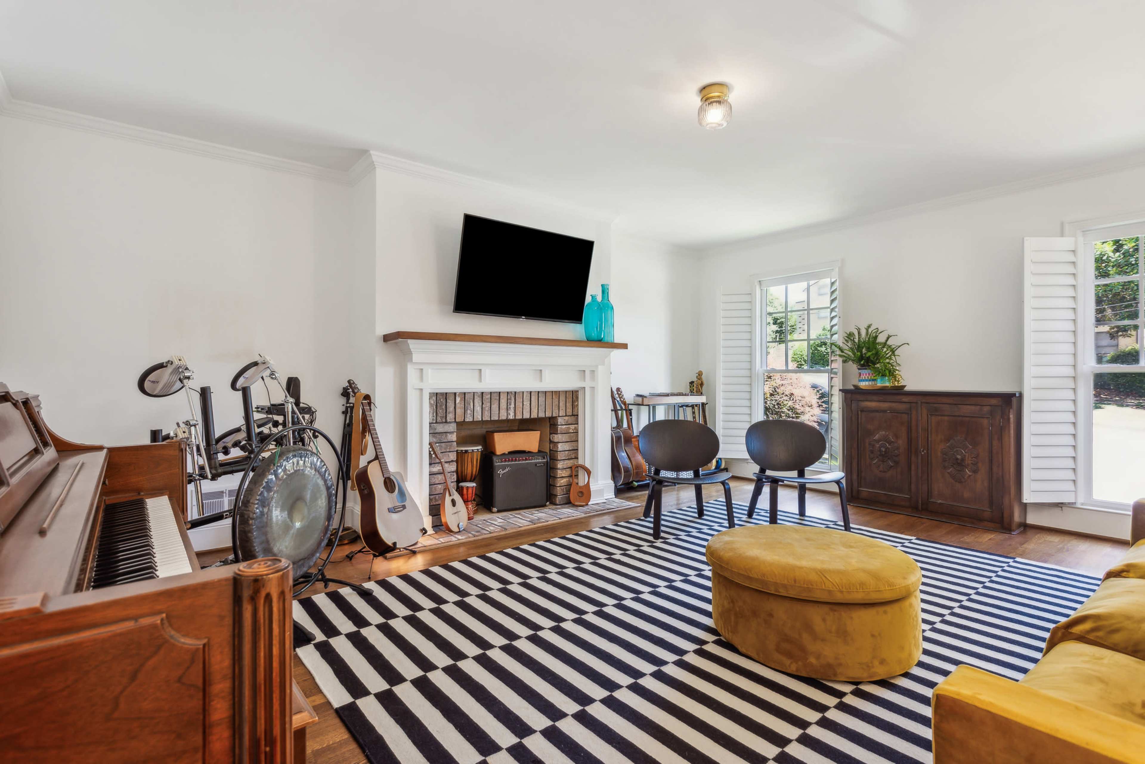 The living room features a piano, a variety of musical instruments, a striped rug, and a cozy yellow ottoman.