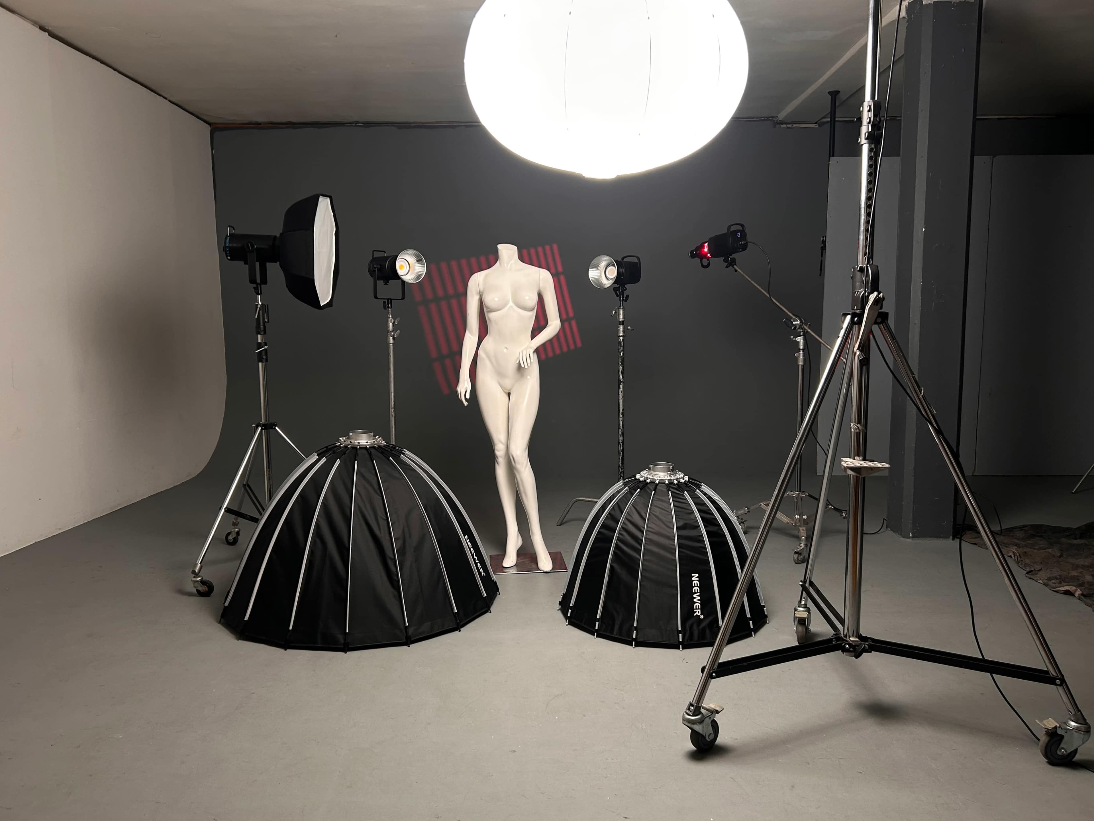 The image shows a photography studio setup featuring a mannequin in the center, flanked by two large softbox lights and a large overhead light.