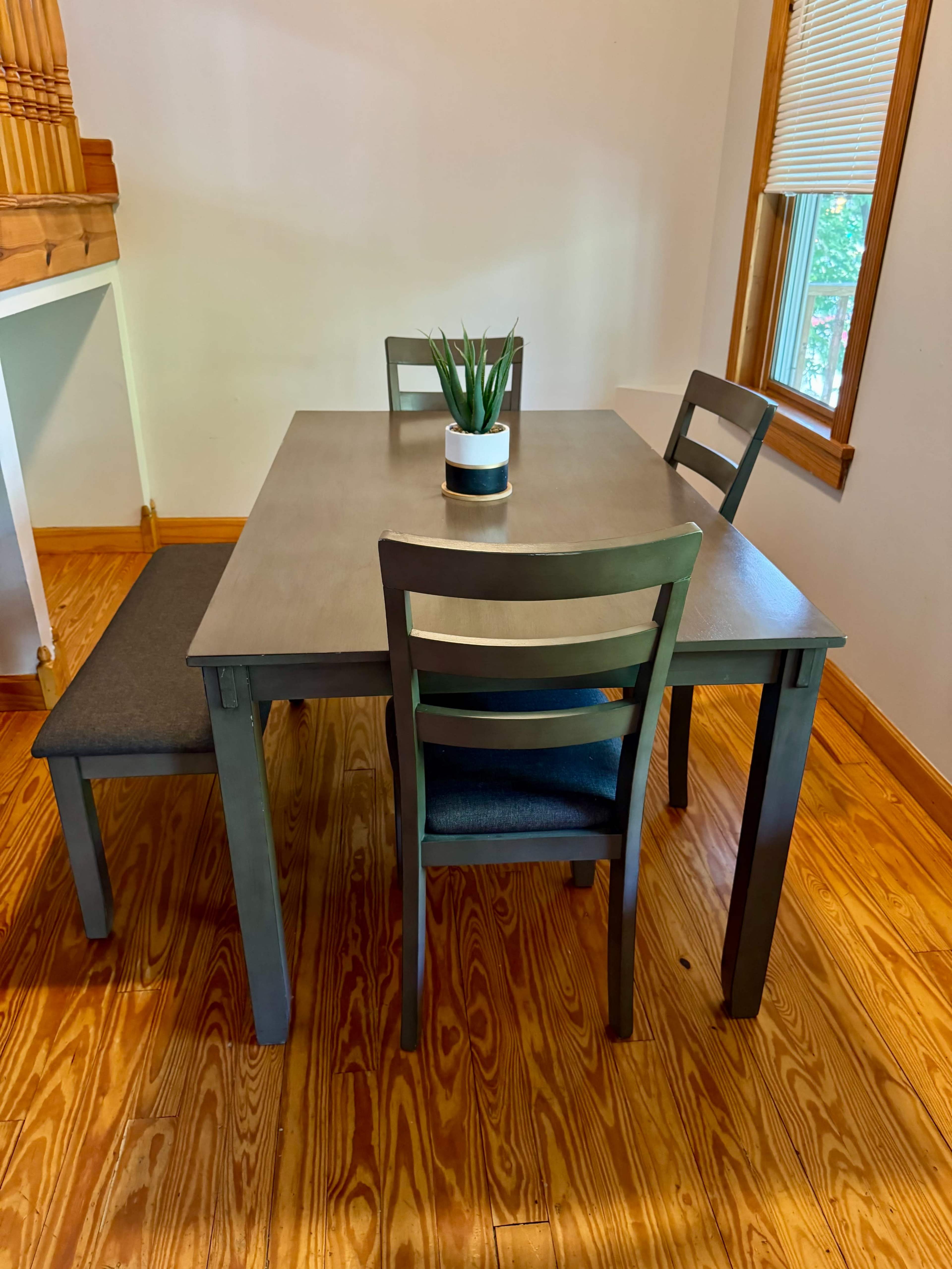 A gray table with two chairs and a bench is positioned in a well-lit dining area with wooden flooring.