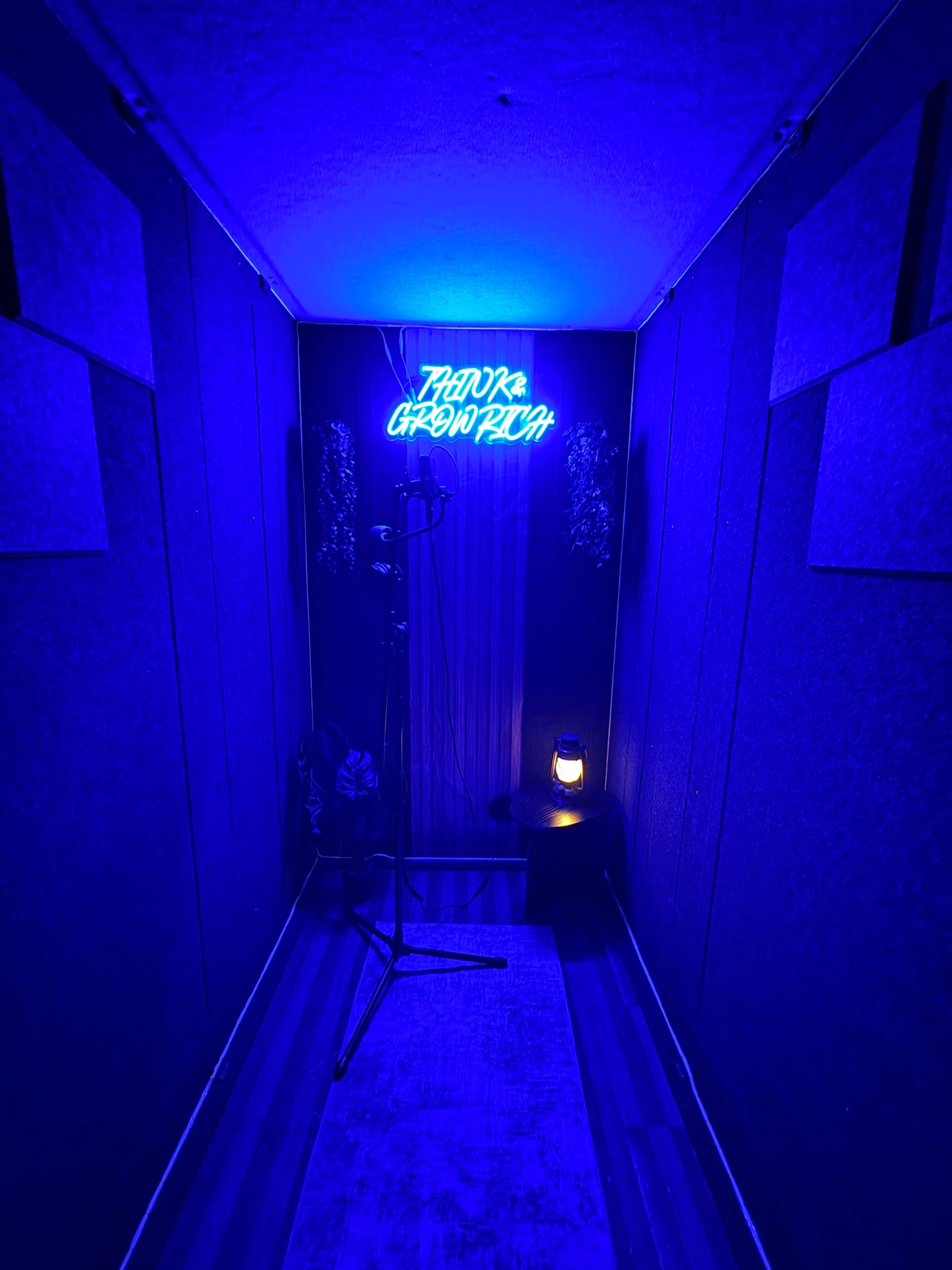 The image shows a dimly lit recording booth with blue walls, a microphone stand, and a decorative neon sign that reads "Thank You, Graphic."