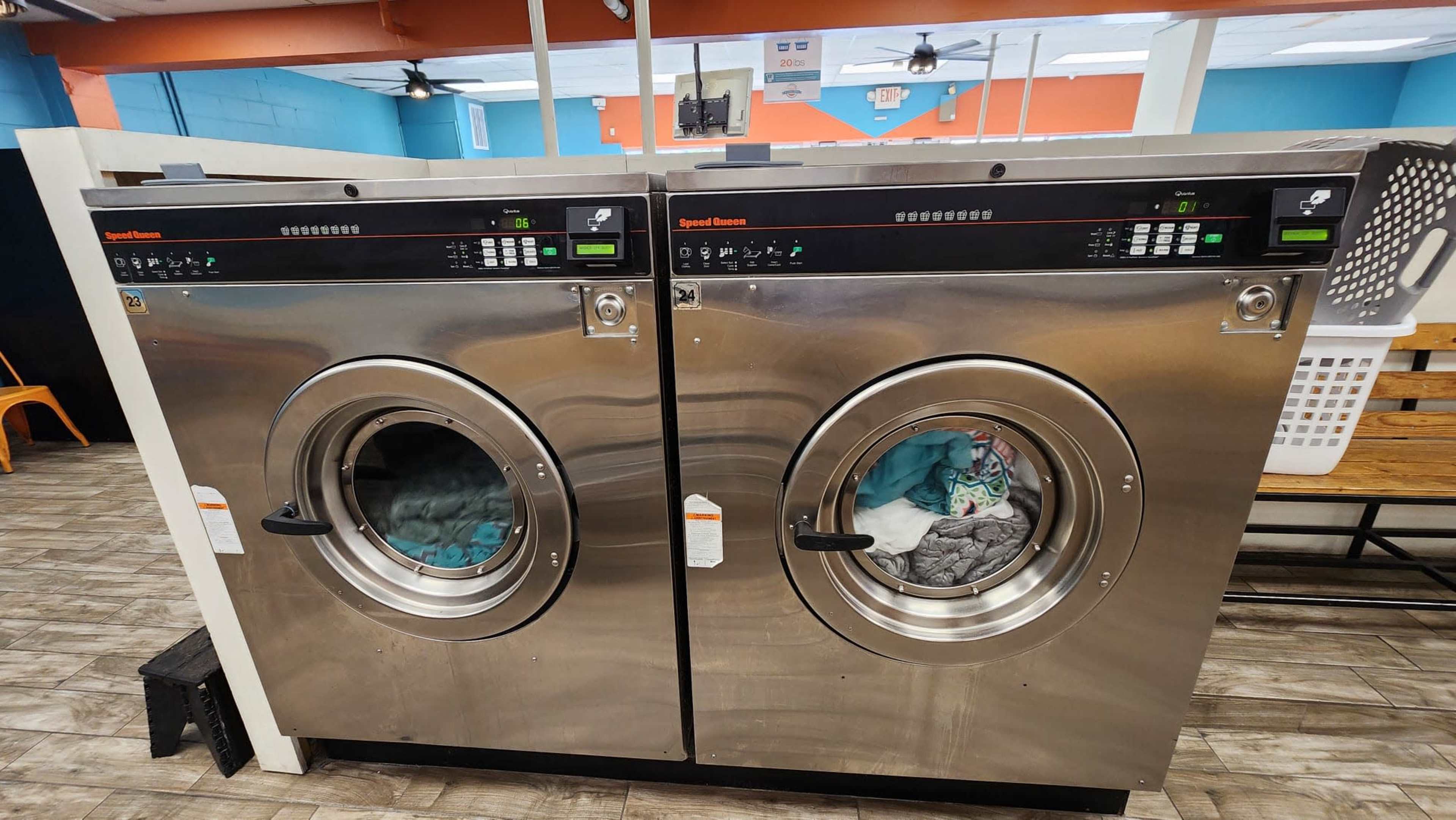 Two stainless steel commercial washing machines side by side in a laundry facility.