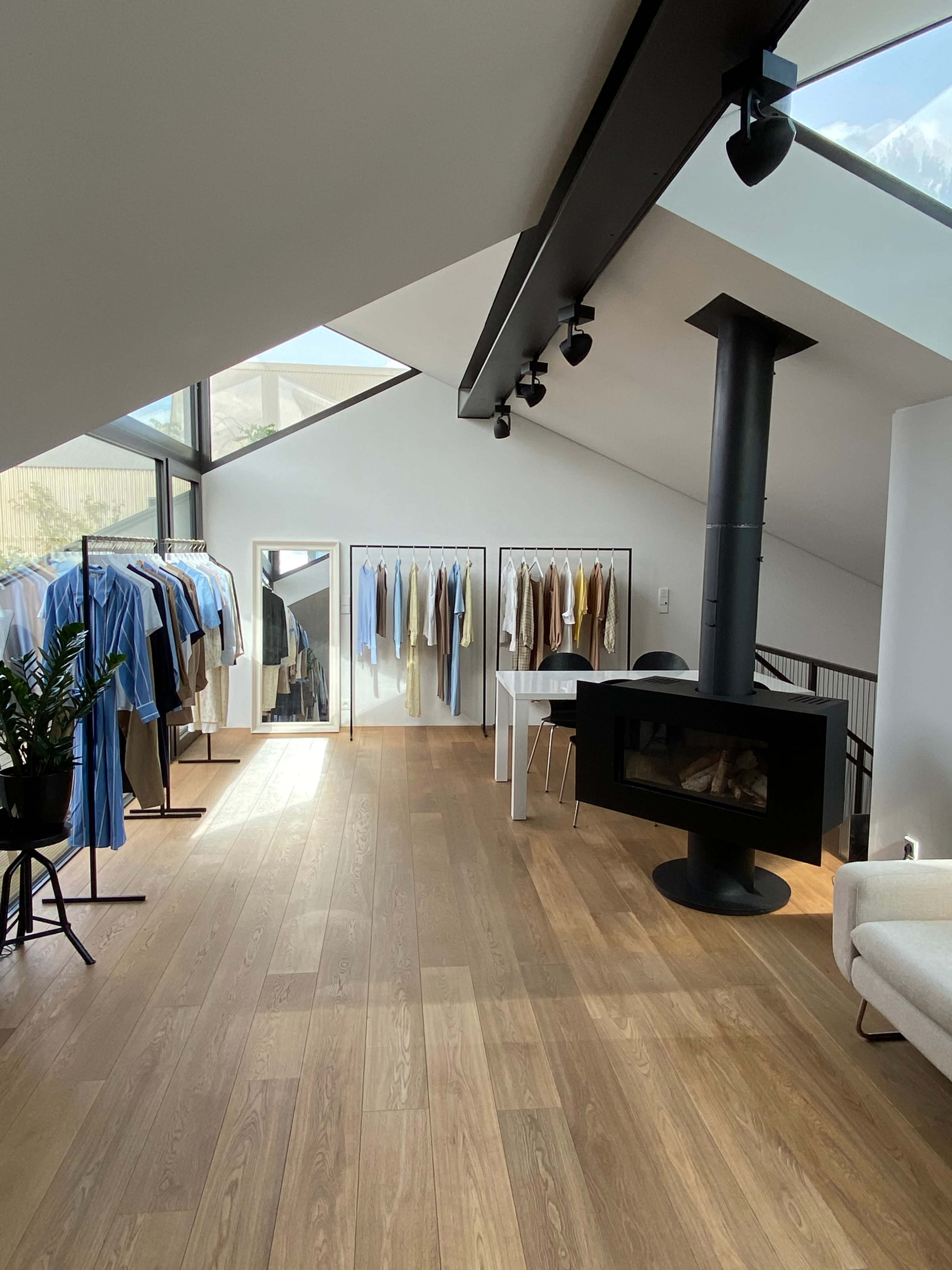 A modern clothing store with a range of garments displayed on racks, a mirror, and a black fireplace in a spacious, light-filled interior.