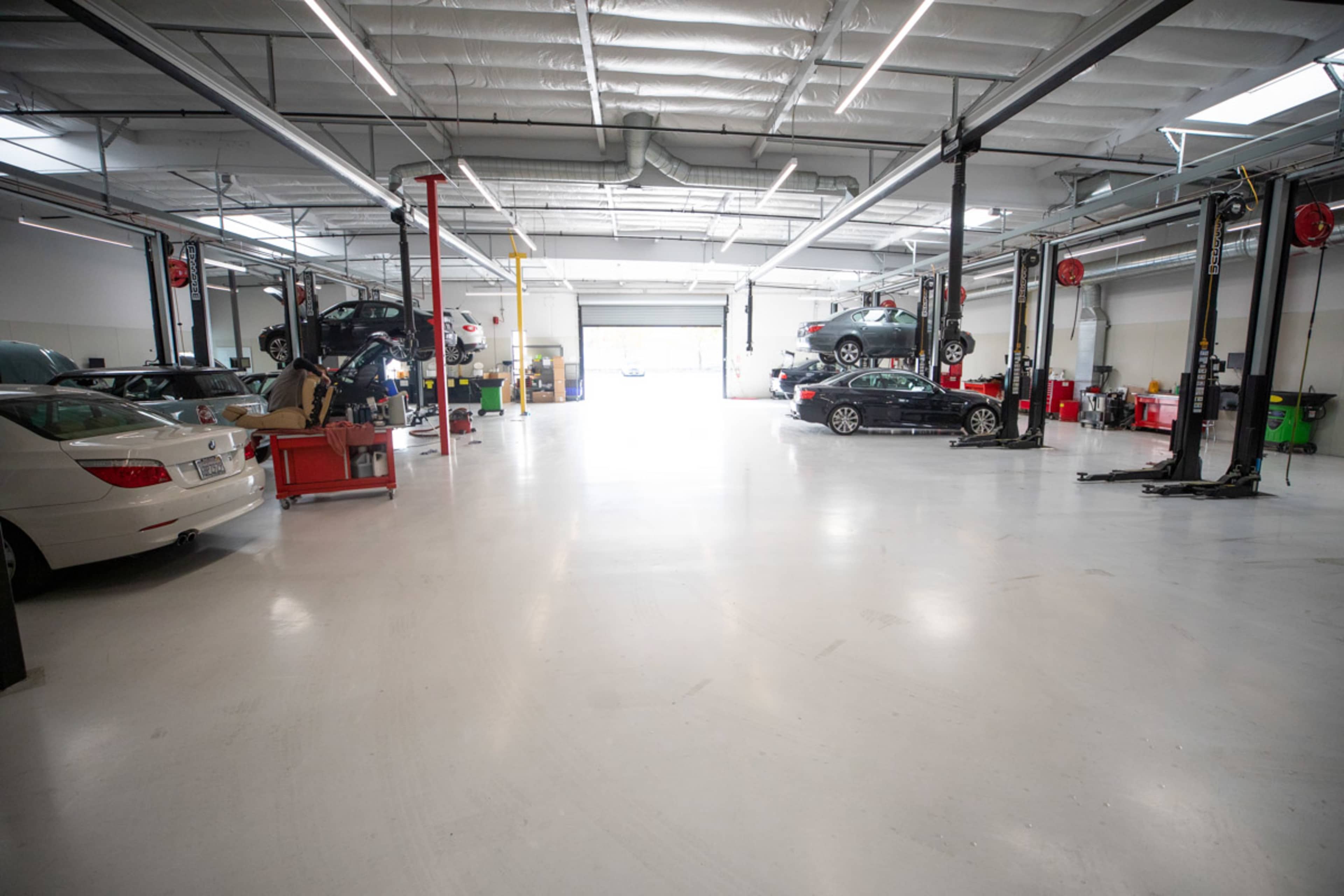 A spacious automotive workshop with multiple cars on lifts and tools organized on the floor.
