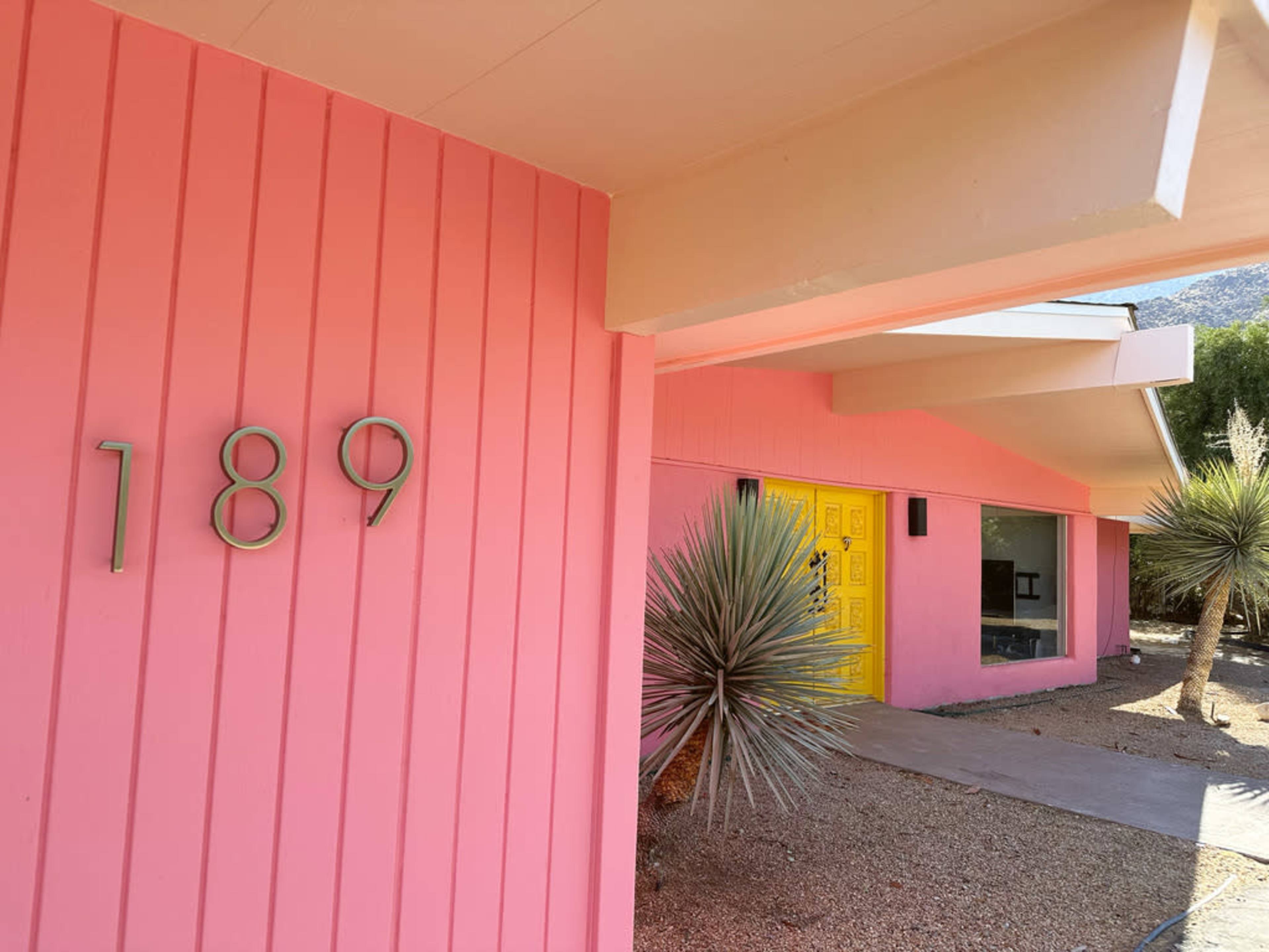 A pink house features the number 189 on its exterior, with a bright yellow door visible in the background.