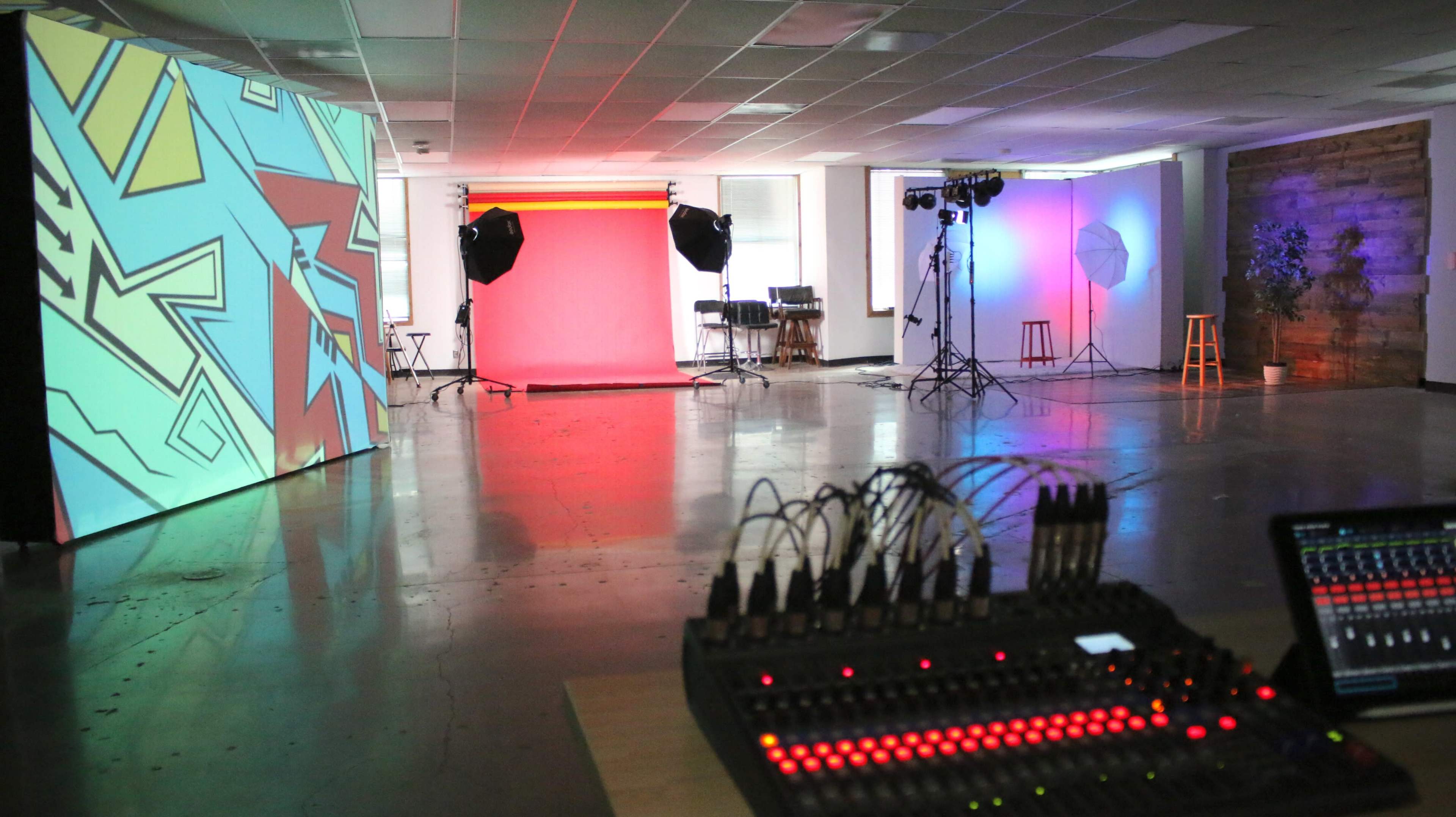 A photography studio with colorful backdrops, lighting equipment, and a sound mixing console in the foreground.