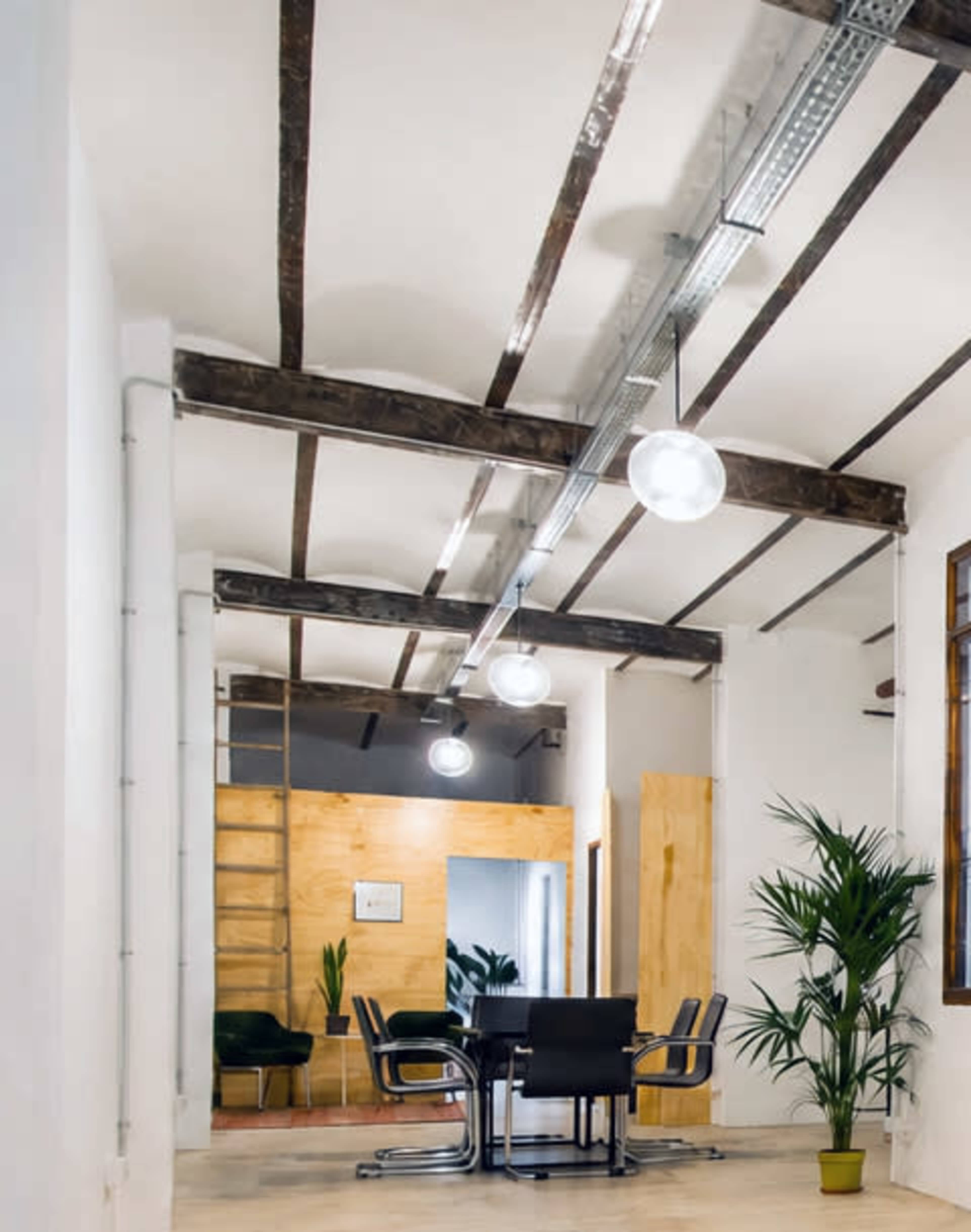 The image shows a modern office space with wooden beams, a conference table, and a decorative plant in the corner.