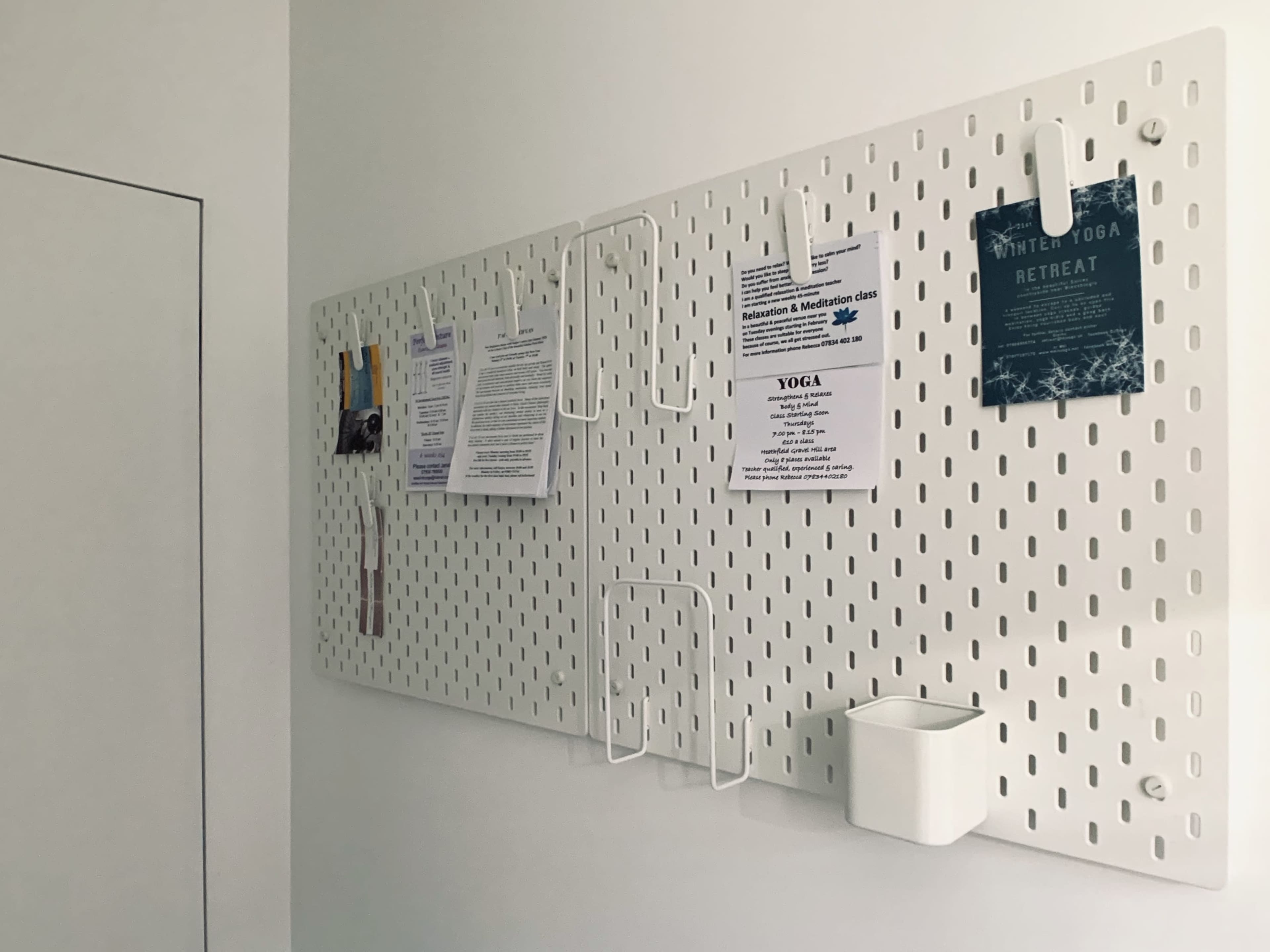 A white pegboard mounted on a wall displays various flyers and documents secured with clips.