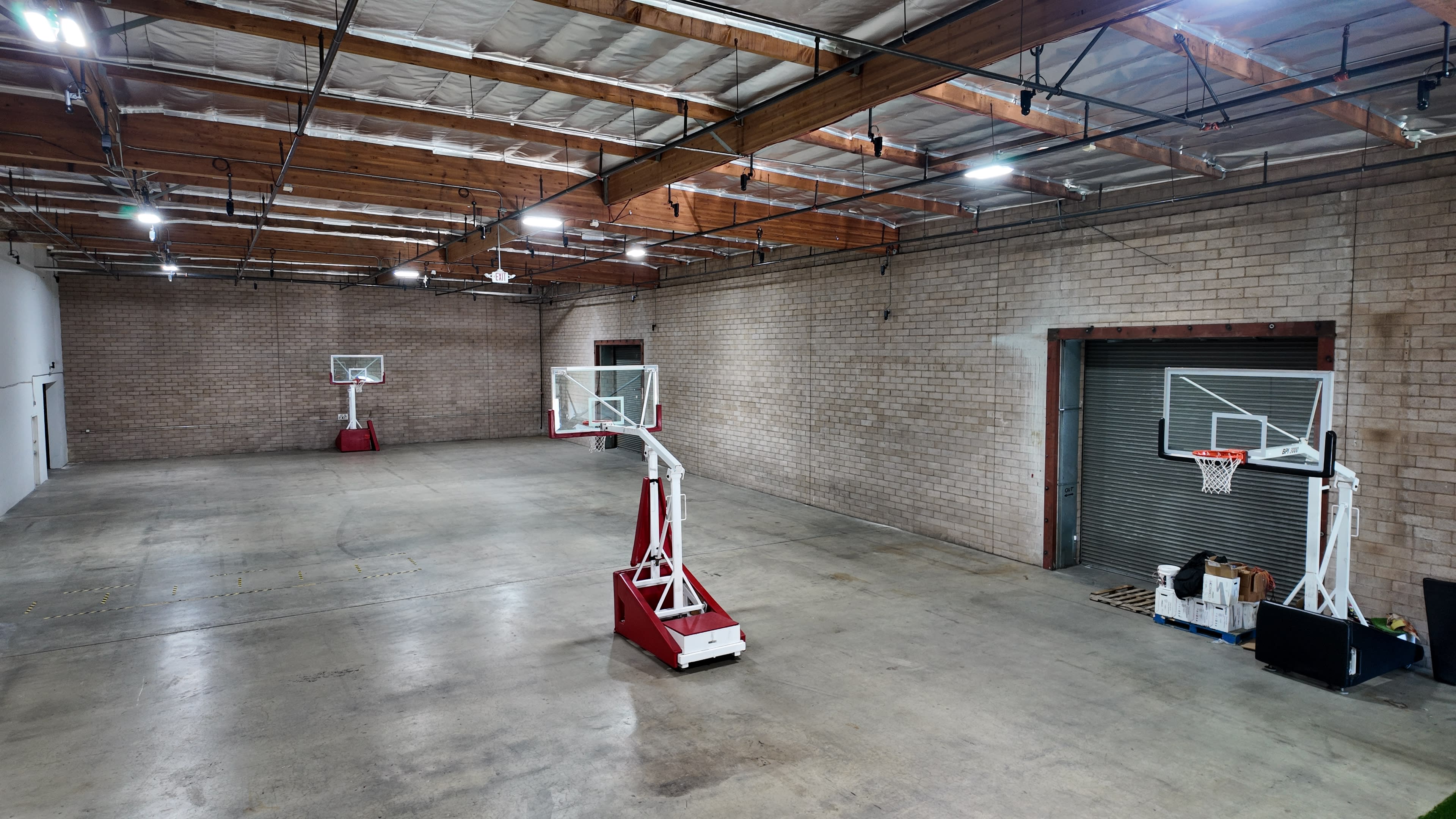 The image shows a spacious indoor basketball court with two basketball hoops at opposite ends and a concrete floor.