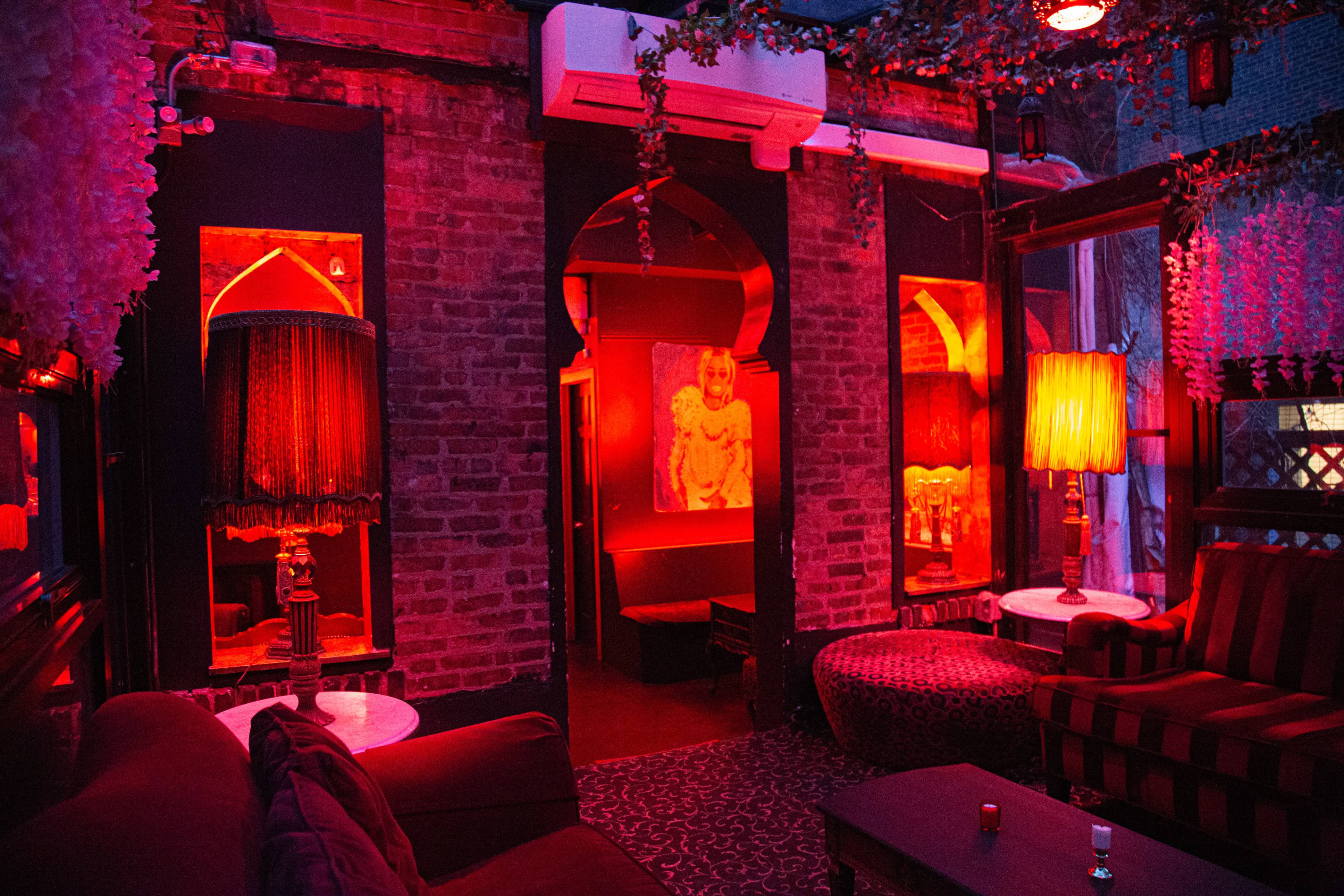 The image shows a dimly lit lounge area with red walls, patterned seating, and decorative lighting.