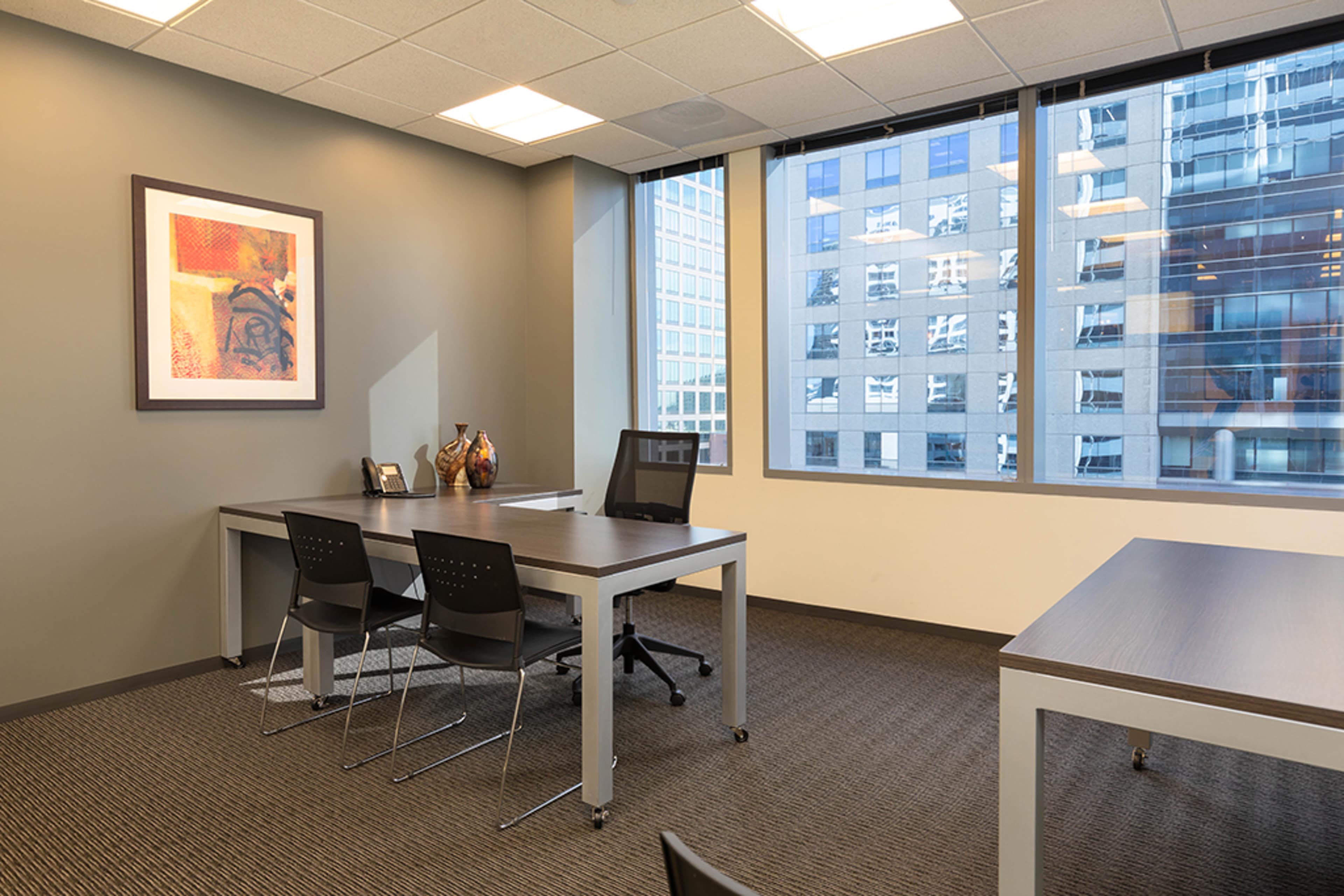 A modern office space featuring a large desk with two chairs and a window offering a view of a city landscape.