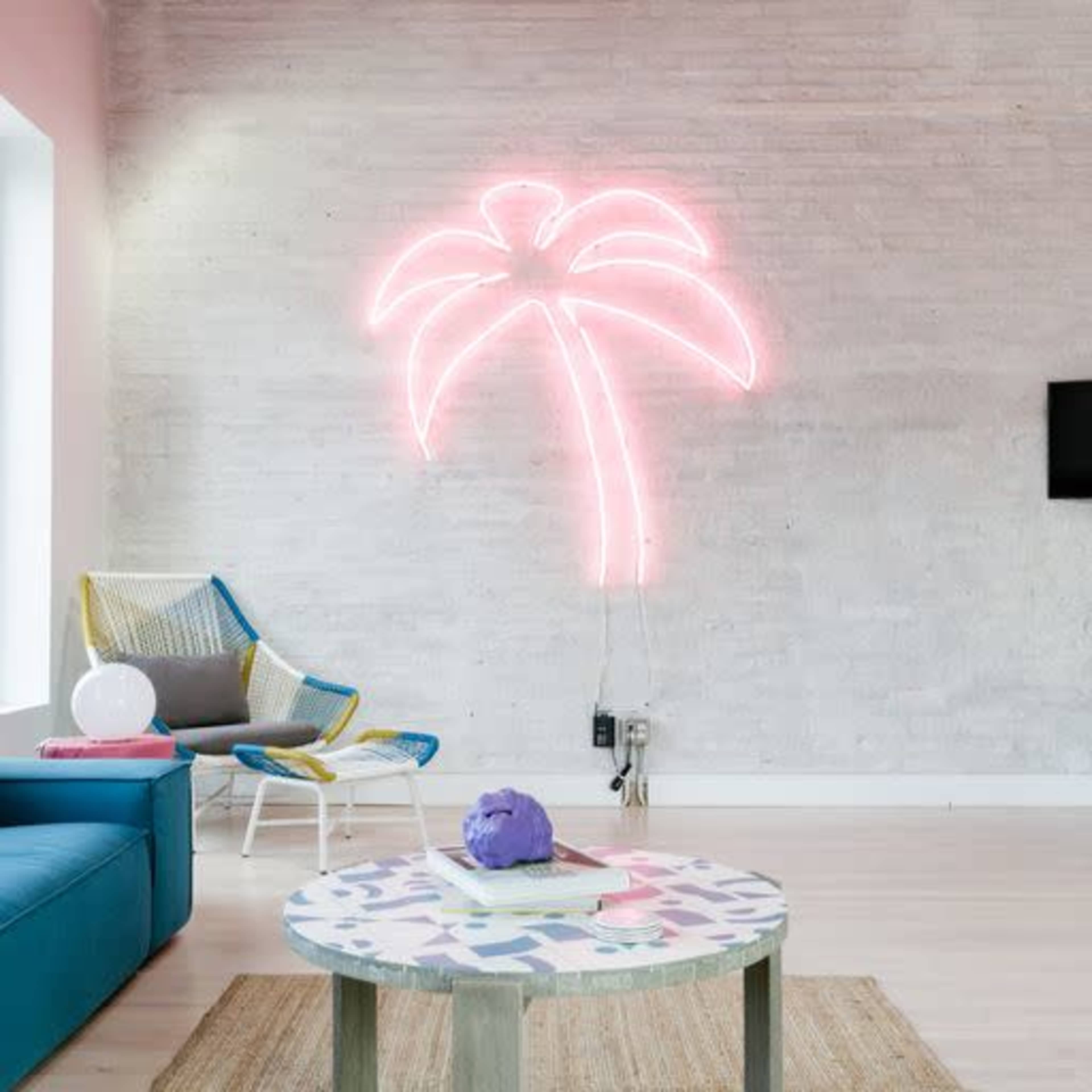A modern living room features a blue sofa, a palm tree neon sign on the wall, and a circular coffee table with a colorful geometric pattern.