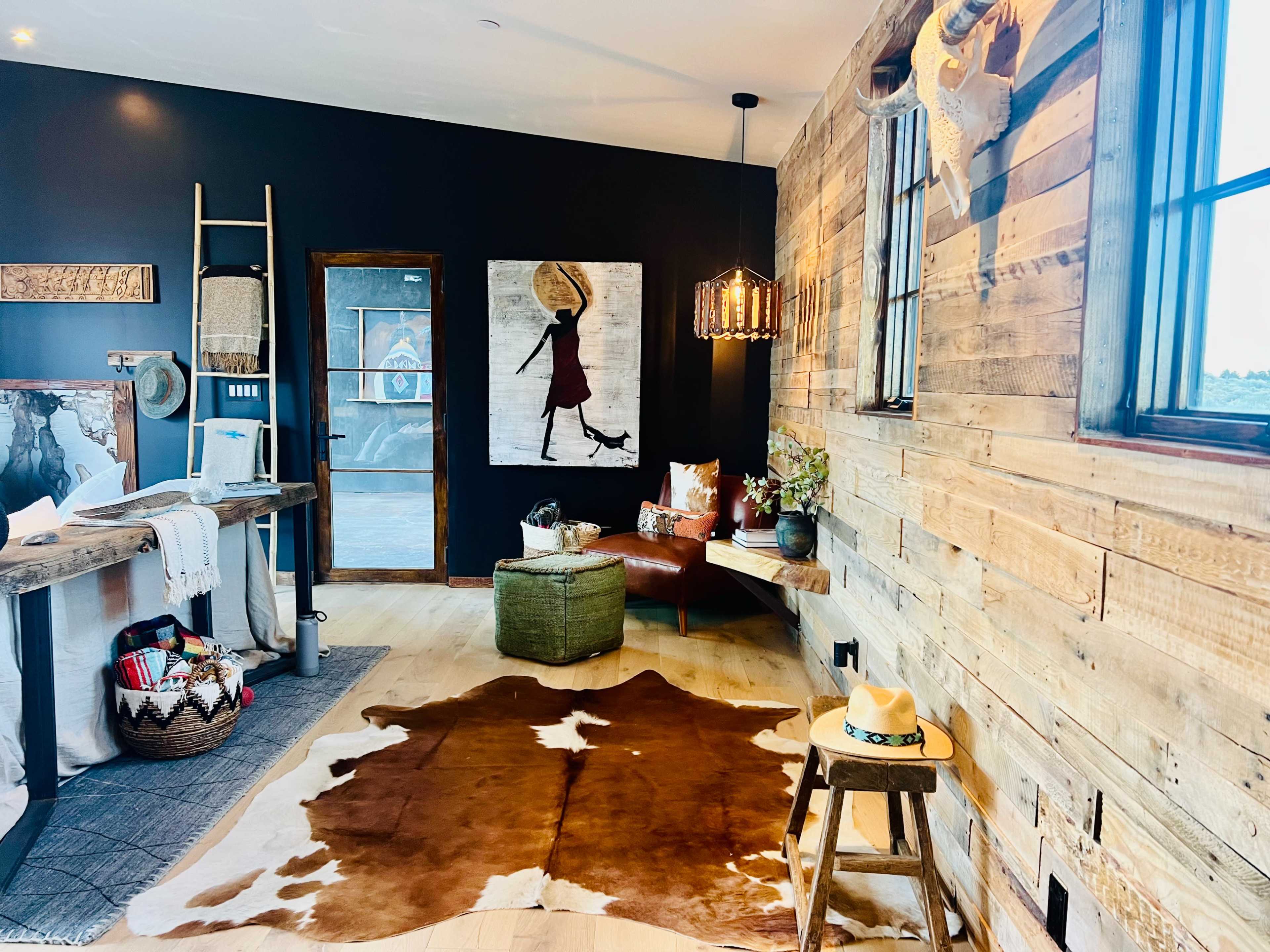 The room features a wooden wall, a cowhide rug on the floor, a comfortable chair, and an art piece depicting a figure carrying a basket.