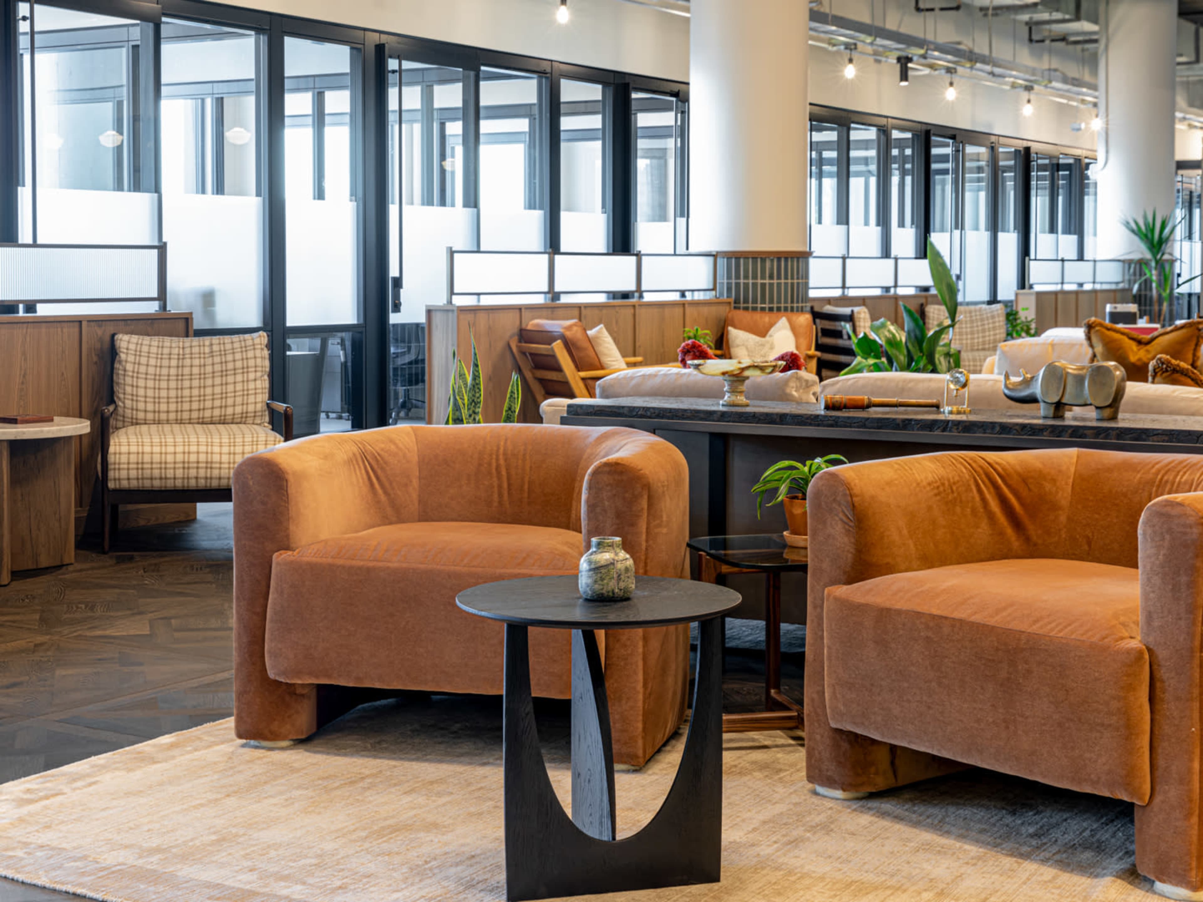A spacious, modern interior featuring brown upholstered armchairs, a black circular table, and large windows allowing natural light.