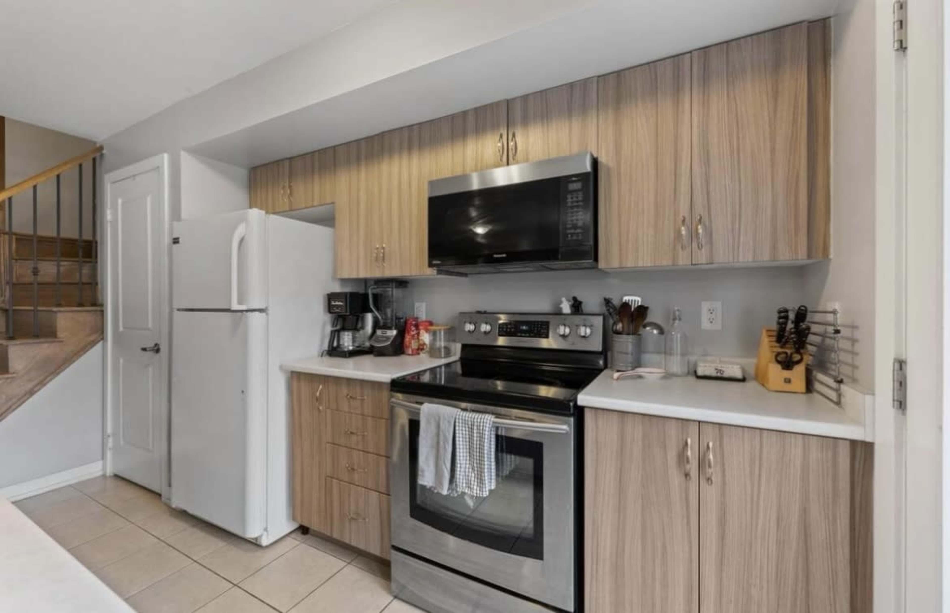 The image shows a modern kitchen with wood cabinetry, stainless steel appliances, and a countertop.