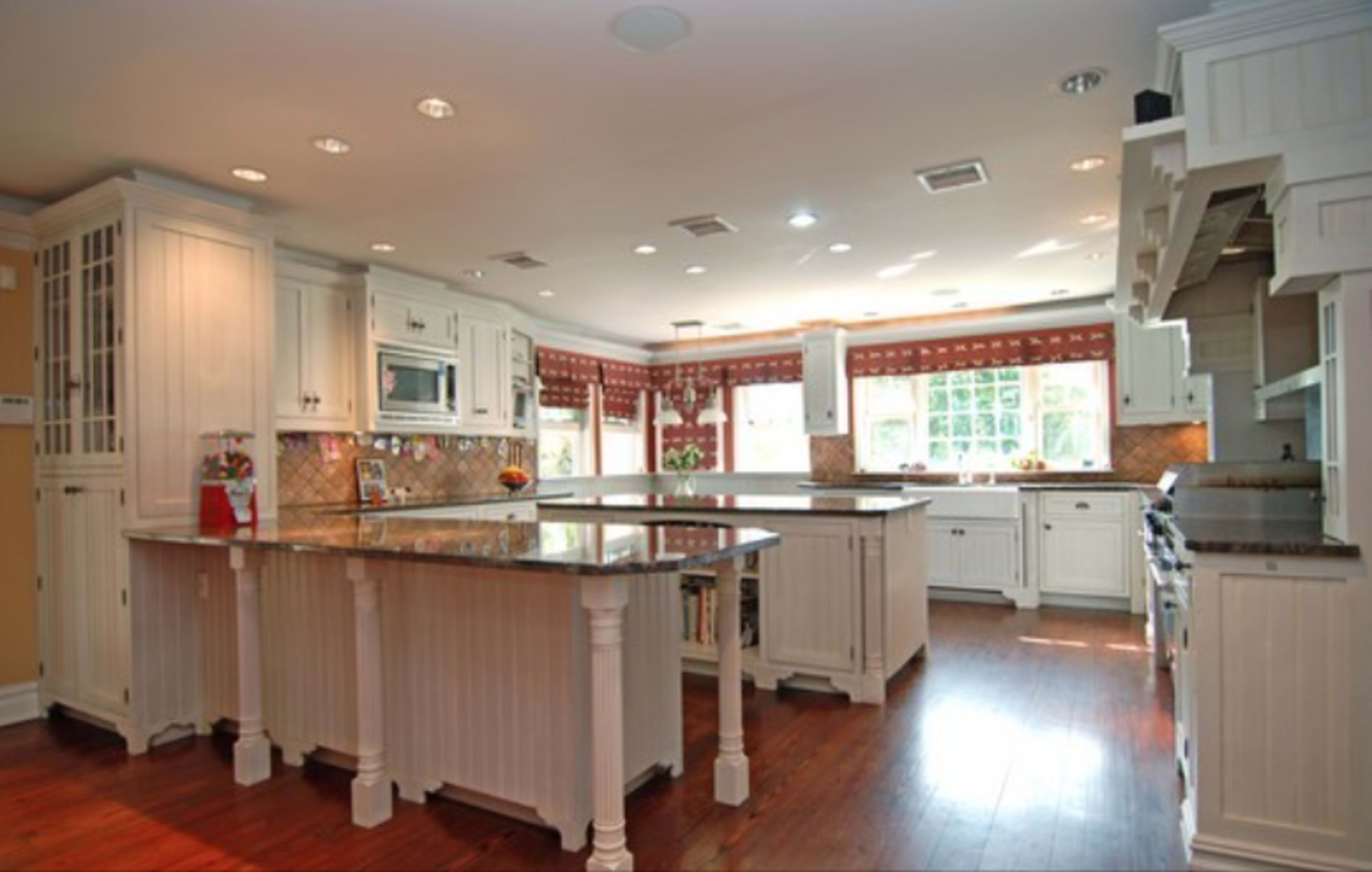 The kitchen features white cabinetry, a central island with marble countertops, and large windows offering natural light.