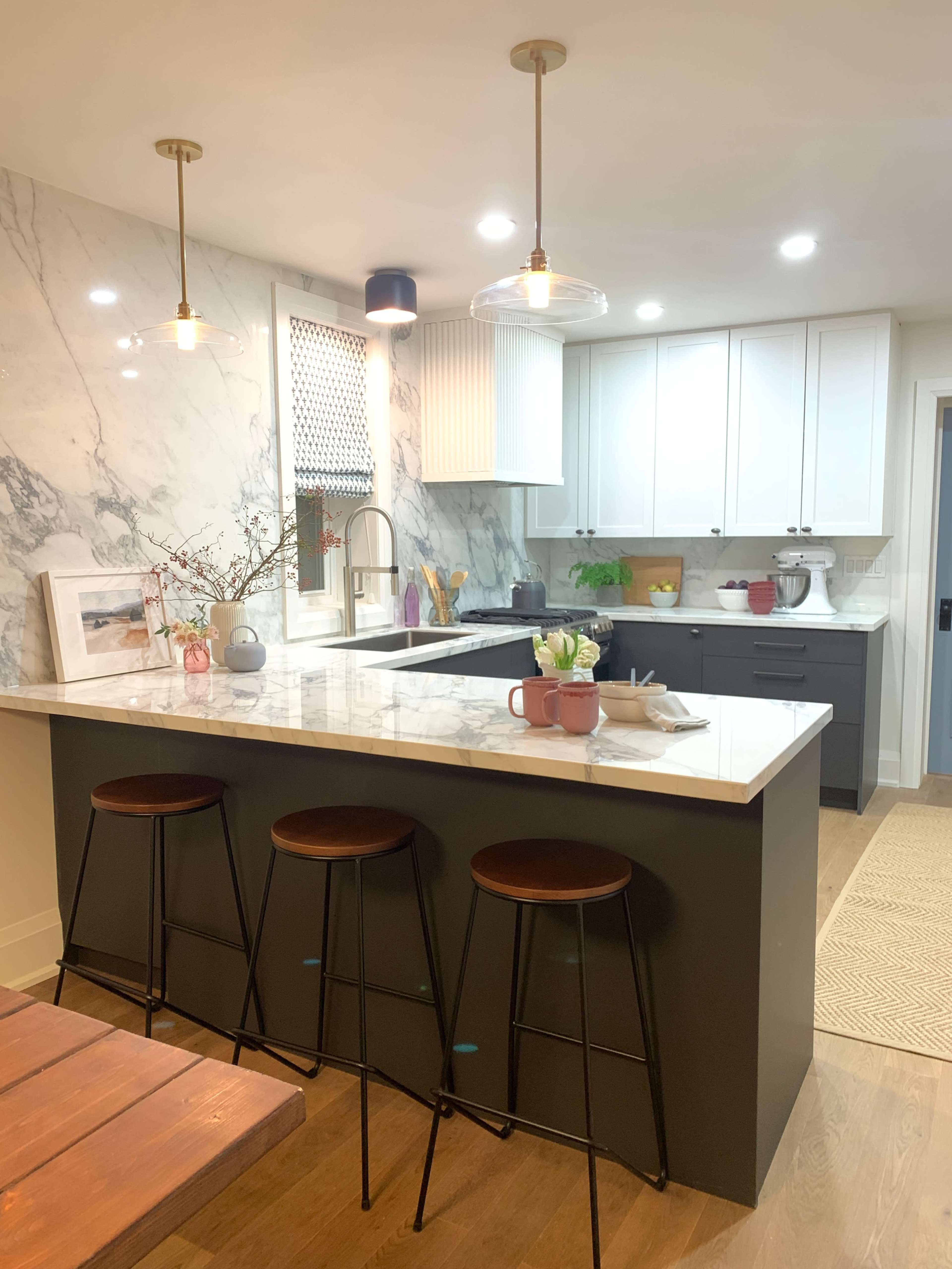 A modern kitchen features a marble backsplash, white cabinets, and a dark island with three bar stools.