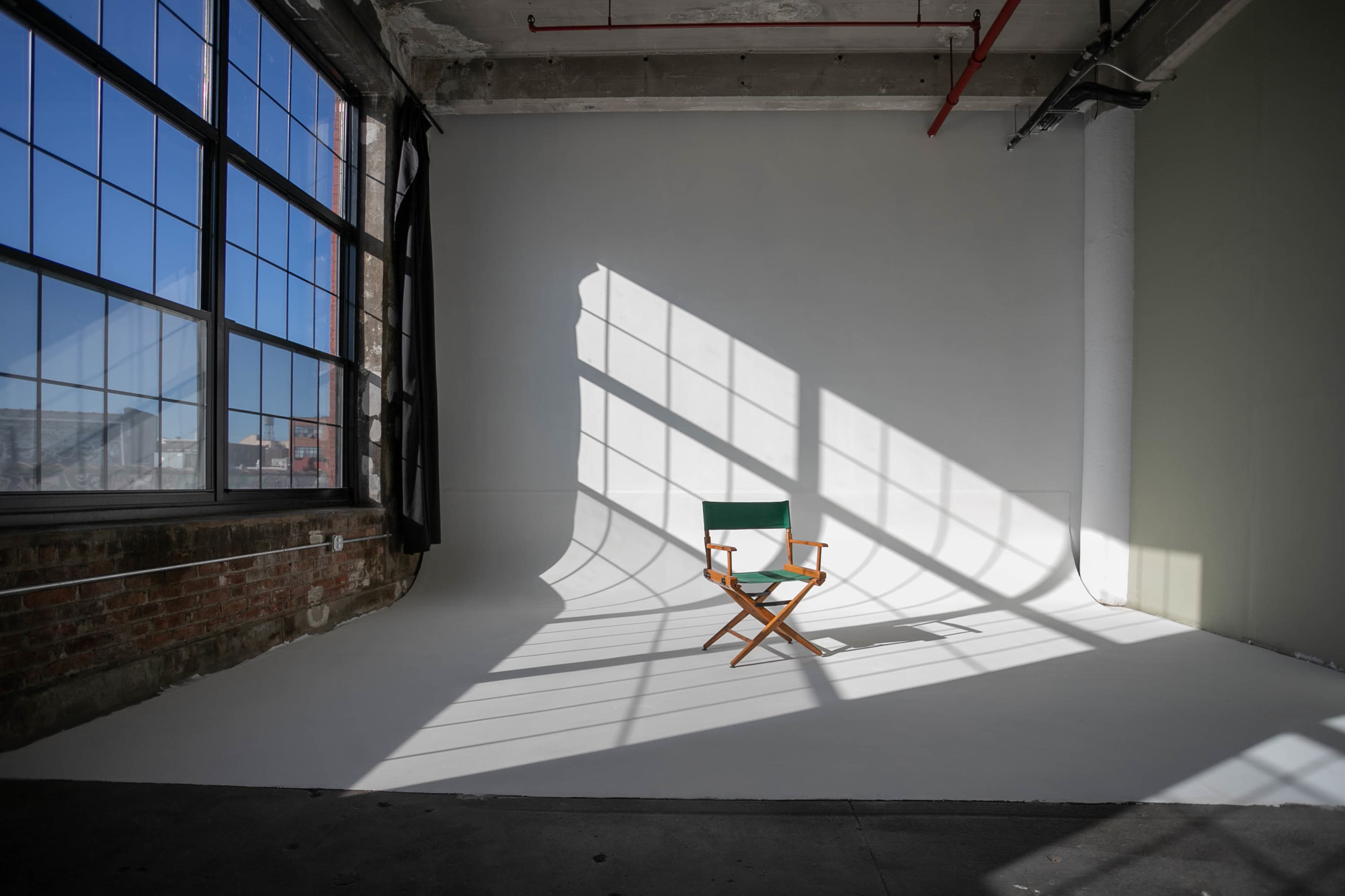 A wooden director's chair sits on a white backdrop, illuminated by sunlight casting long shadows through large windows.