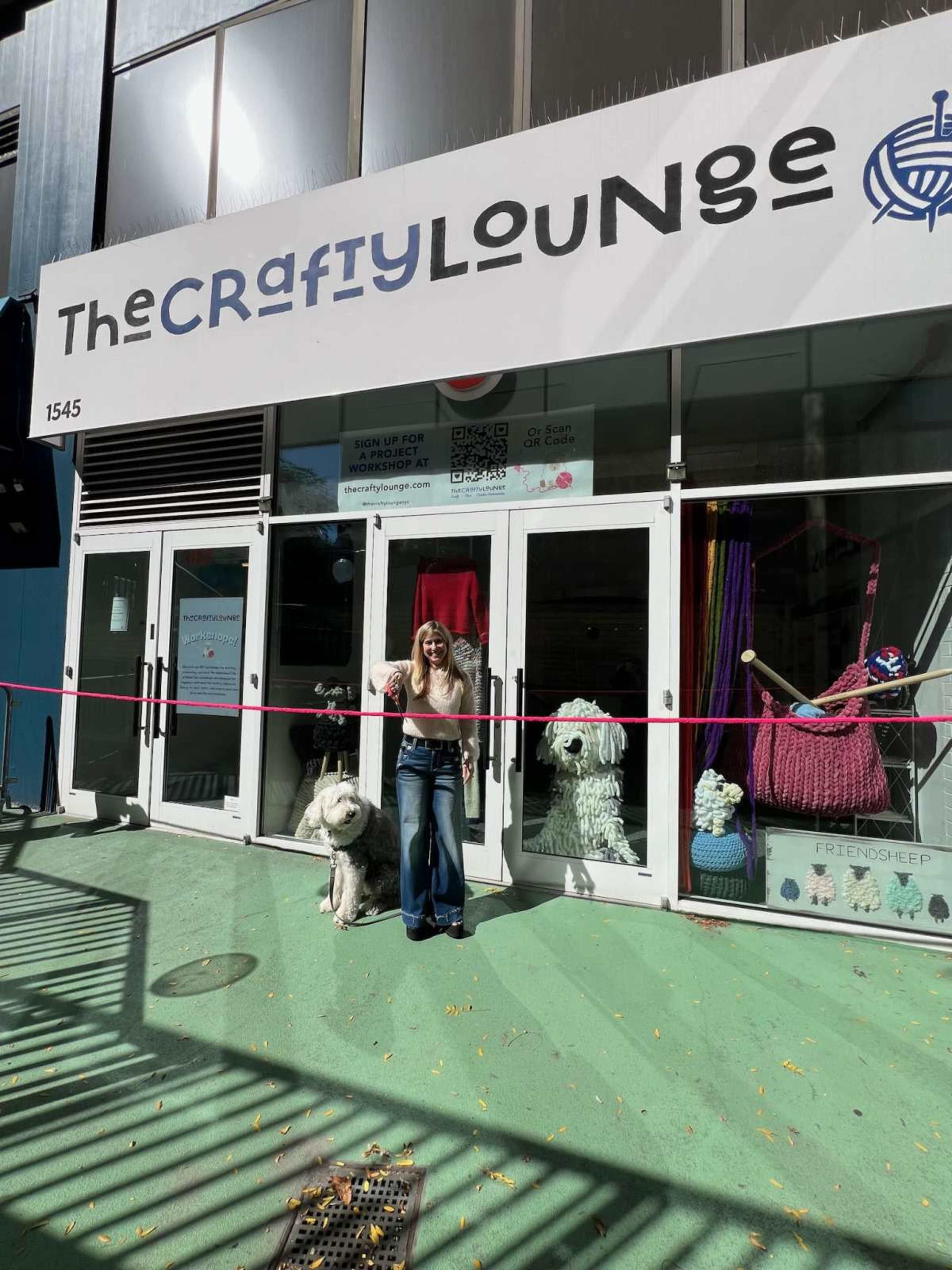A woman stands in front of The Crafty Lounge, which features large yarn creations and a sign above the entrance.