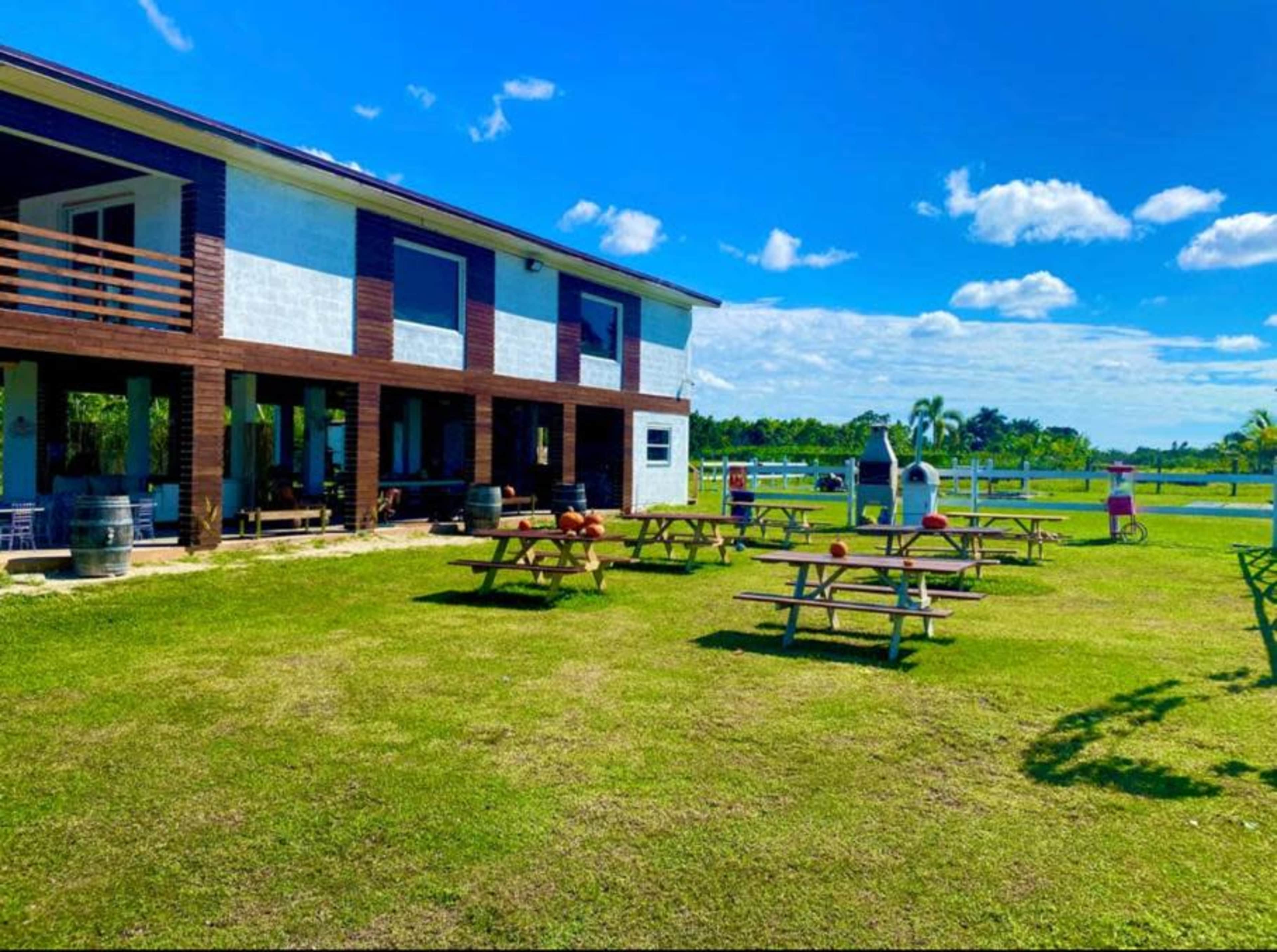 A two-story building with outdoor picnic tables and a grassy area, surrounded by palm trees under a clear blue sky.