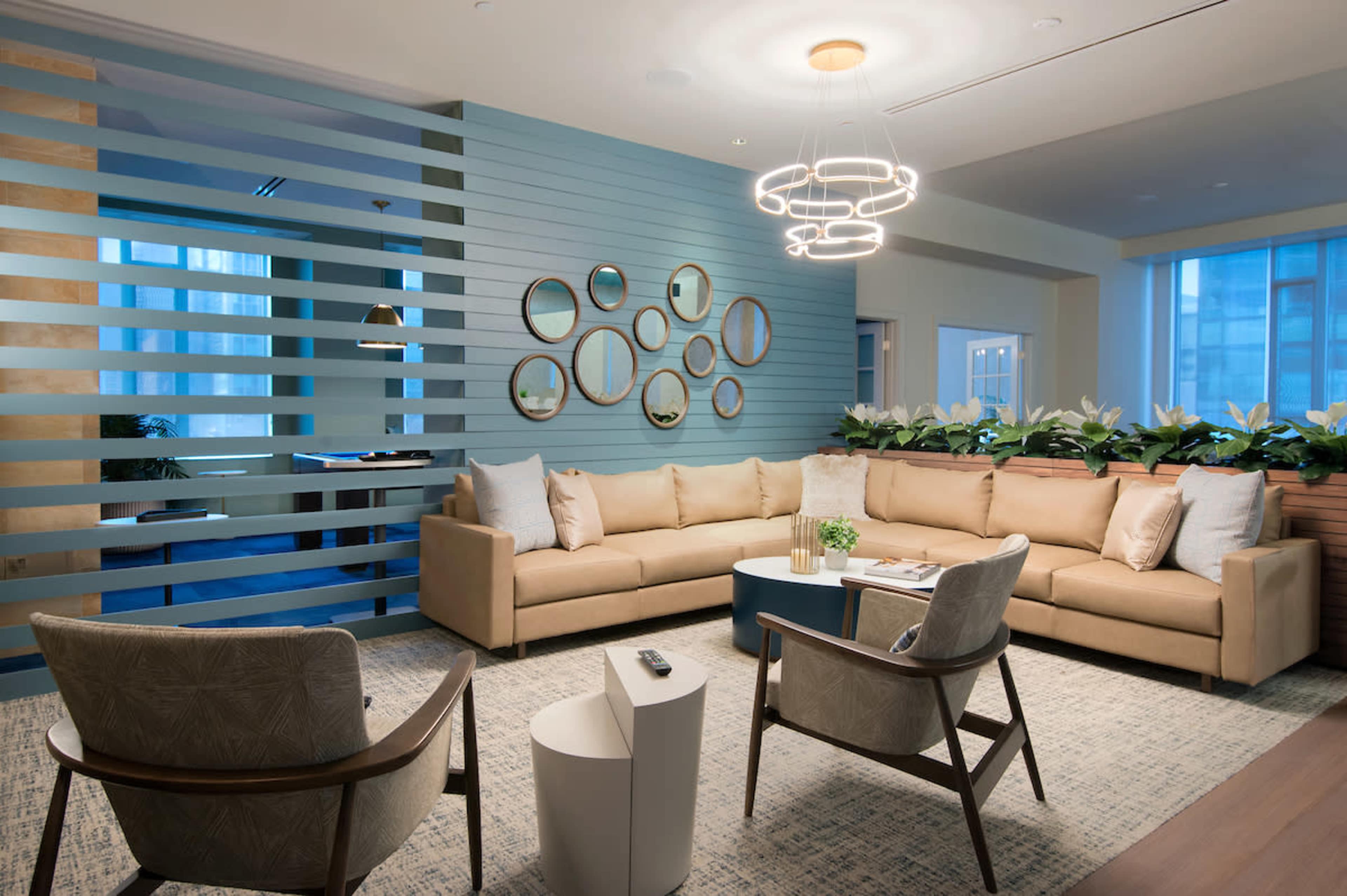 A modern lounge area features a beige sectional sofa, circular mirrors on the wall, and a round coffee table, illuminated by a contemporary light fixture.