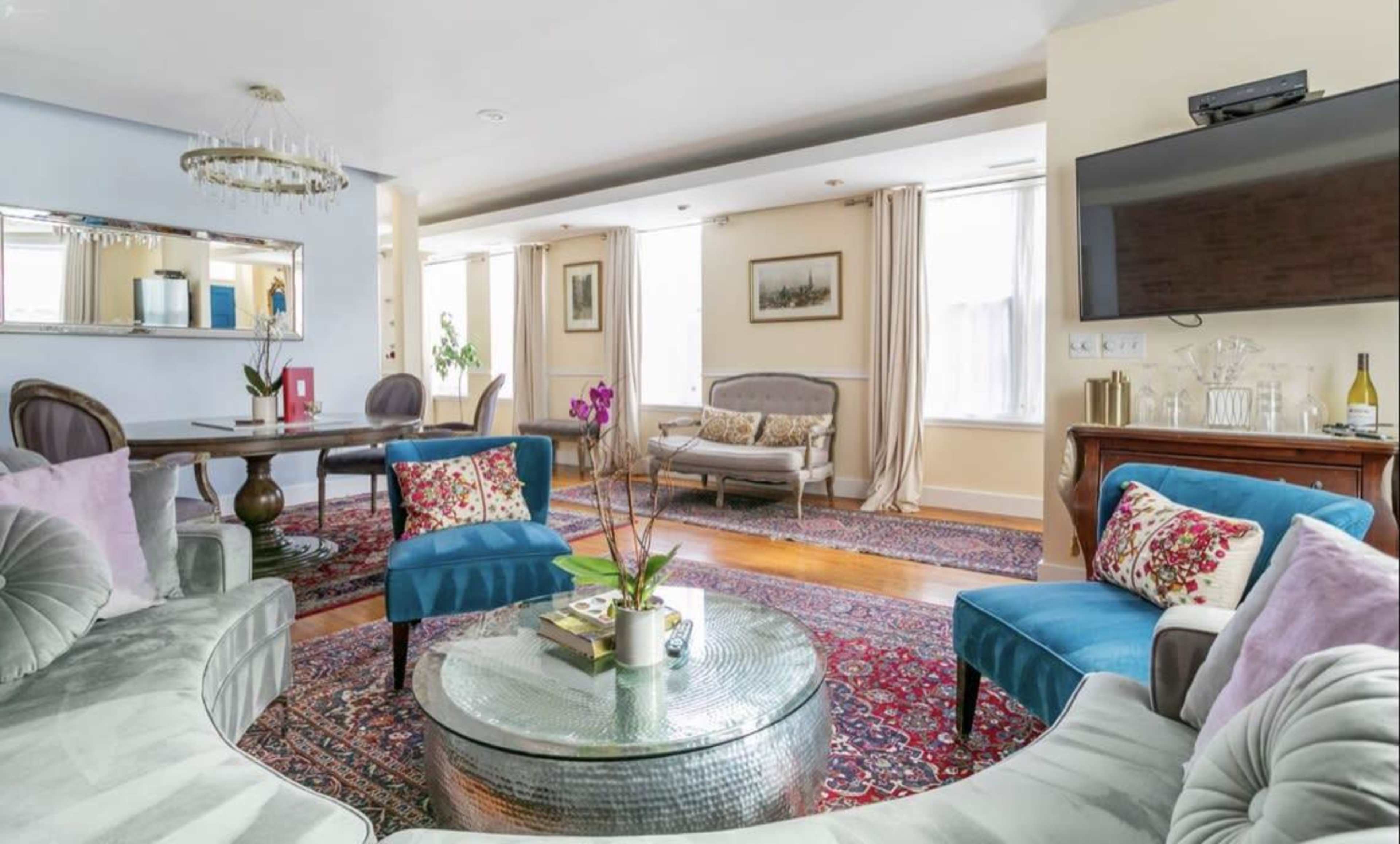 A well-furnished living space featuring a circular sofa, a glass coffee table, and a dining area with a wooden table.