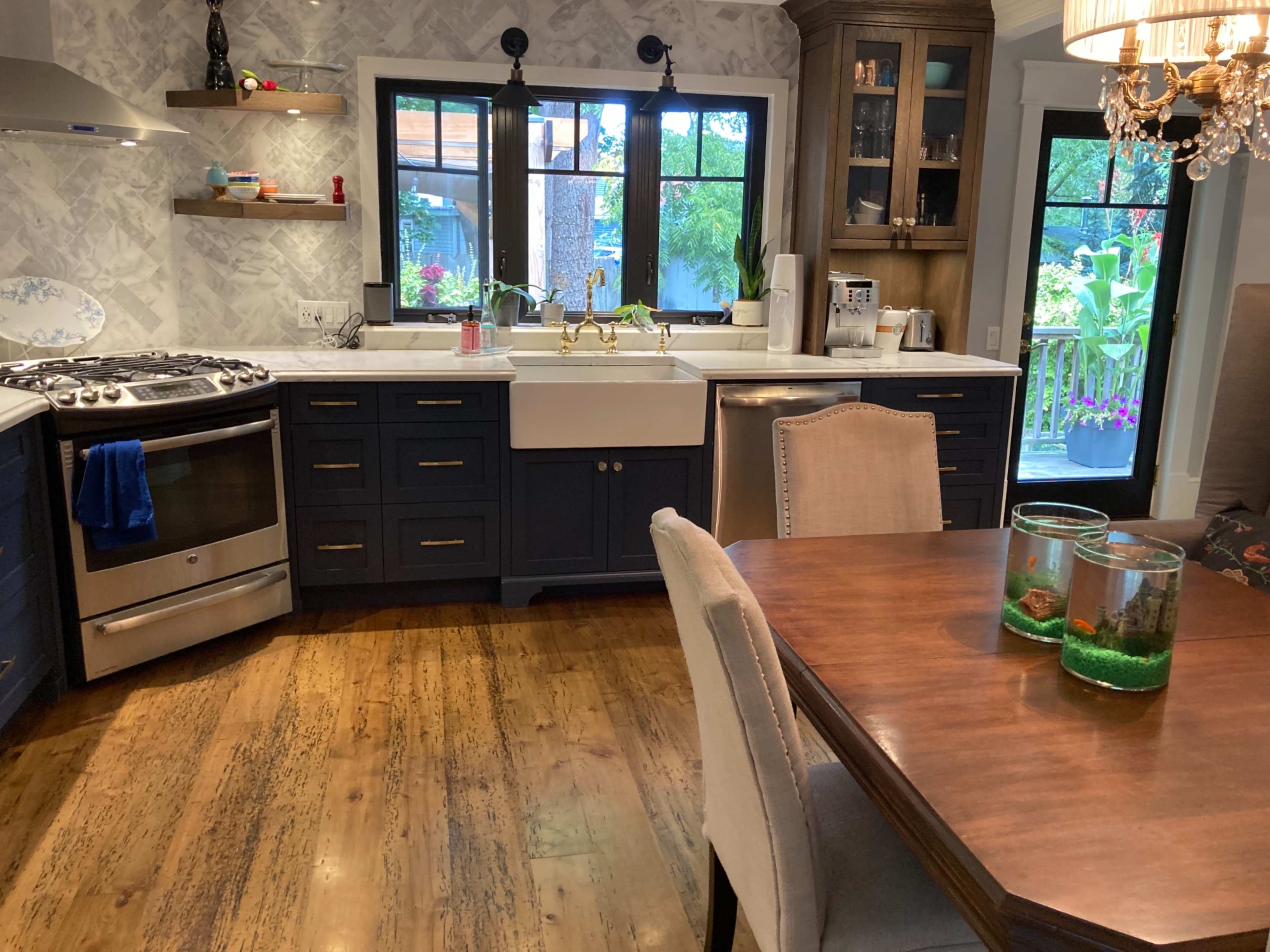 A kitchen with blue cabinets, a farmhouse sink, a stainless steel stove, and a wooden dining table with two aquariums.