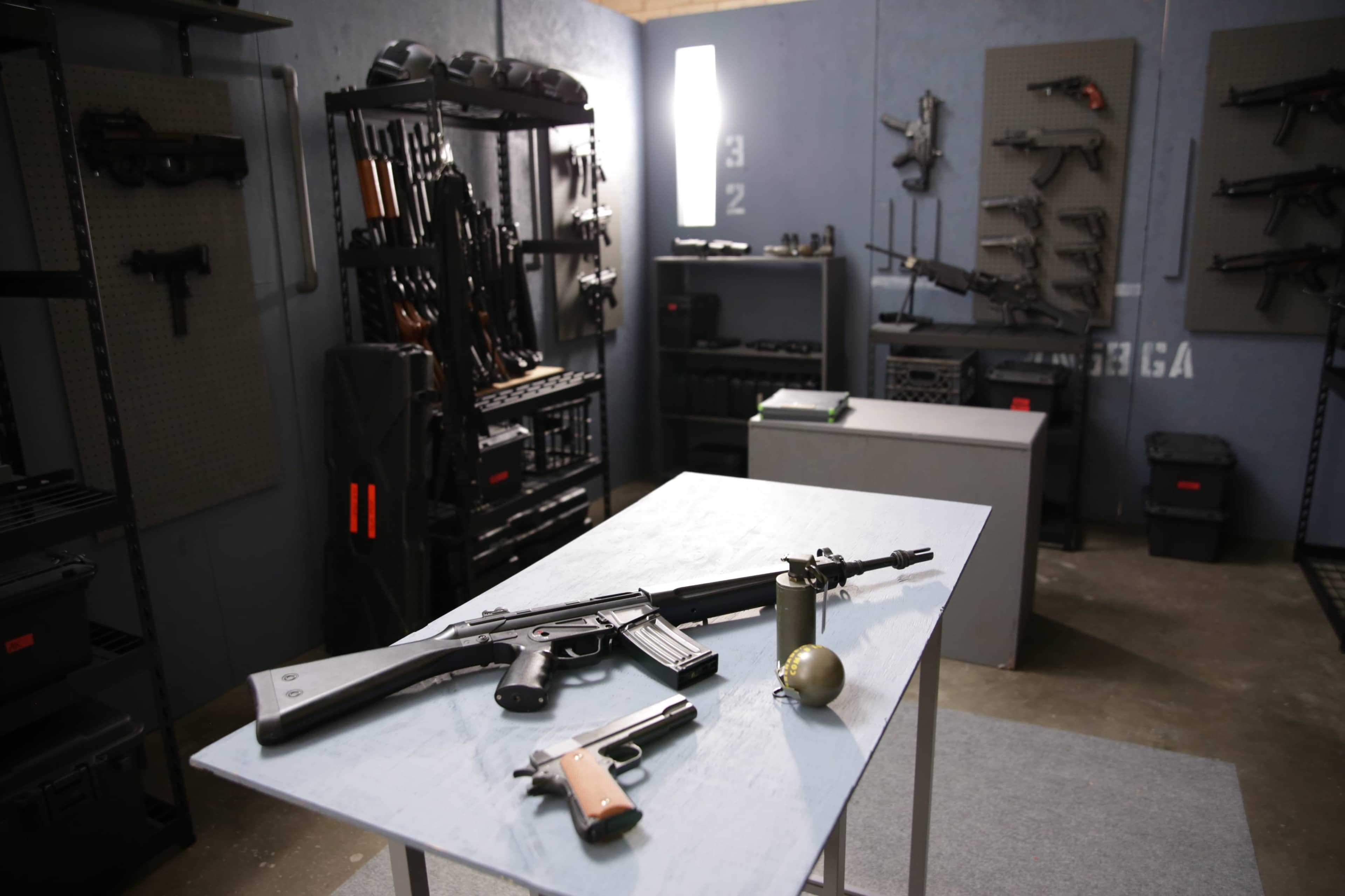 The image shows a room filled with various firearms and ammunition displayed on racks and tables.