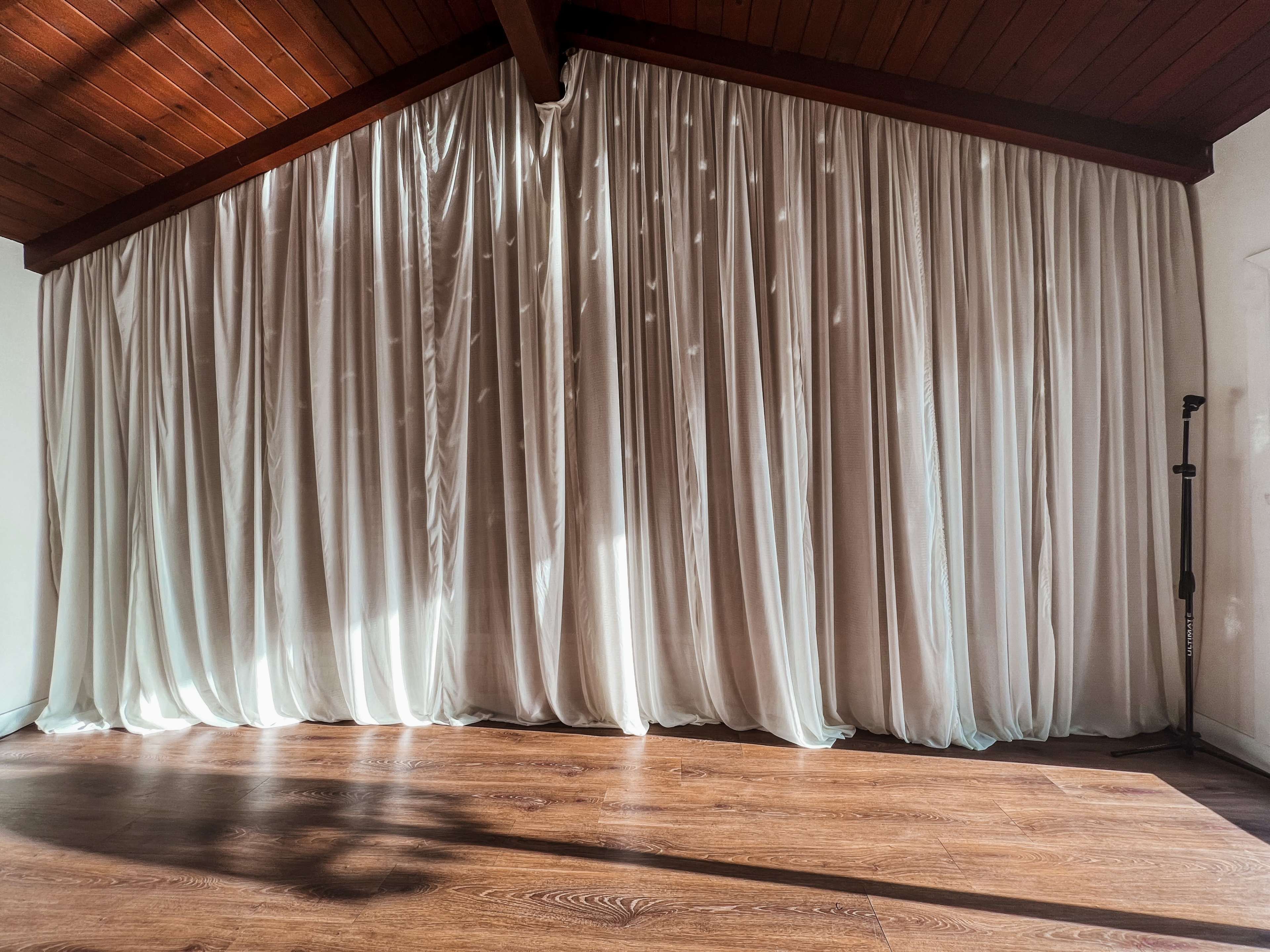 A room features floor-to-ceiling sheer curtains that drape over a wooden floor.